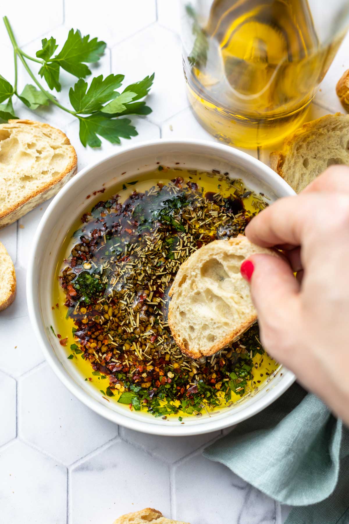 hand dipping a slice of bread into dipping oil with herbs and balsamic vinegar