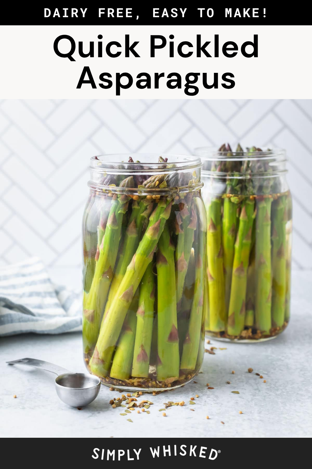 Two glass jars filled with pickled asparagus spears and aromatic spices sit invitingly on a marble surface. A metal measuring spoon and scattered spices add a touch of rustic charm. Text above reads, “Quick Pickled Asparagus.”.