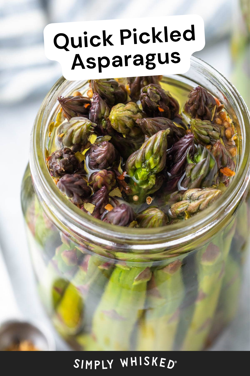 A jar filled with pickled asparagus spears in brine, with seasonings floating on top. The label above the jar reads Quick Pickled Asparagus, highlighting the crisp and tangy flavor of pickled asparagus. The bottom says Simply Whisked.