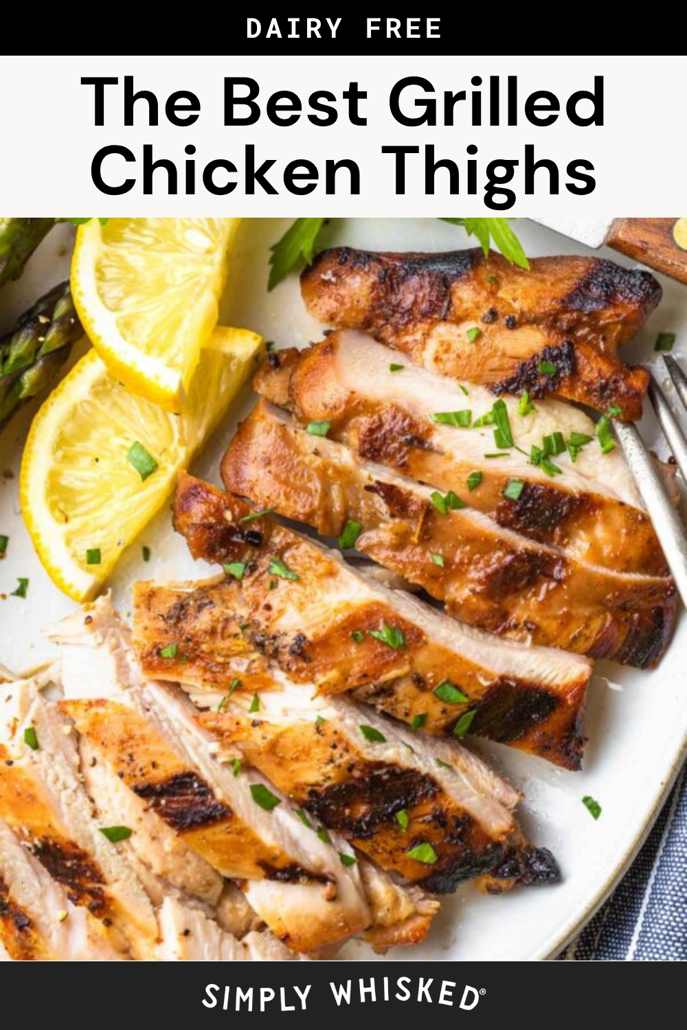 Sliced grilled chicken thighs, perfectly seasoned and char-grilled, are garnished with chopped herbs and served with lemon wedges and asparagus on a white plate. The text reads, “The Best Grilled Chicken Thighs - Dairy Free.”.