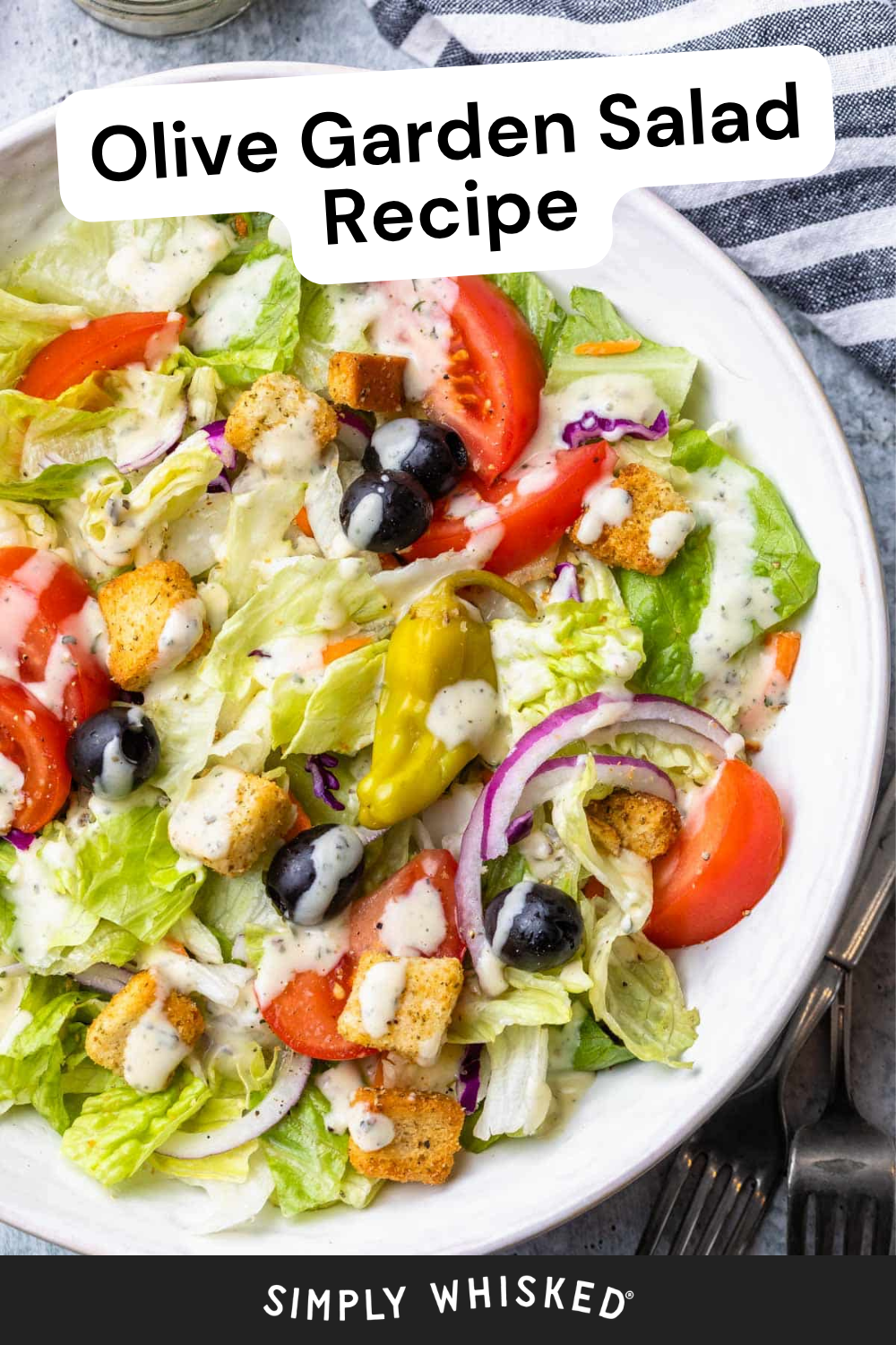 A vibrant bowl of Olive Garden salad featuring crisp lettuce, juicy tomatoes, black olives, red onions, crunchy croutons, tangy pepperoncini, and a creamy dressing is showcased with a fork nearby. Text reads “Olive Garden Salad Recipe” and “Simply Whisked.”.