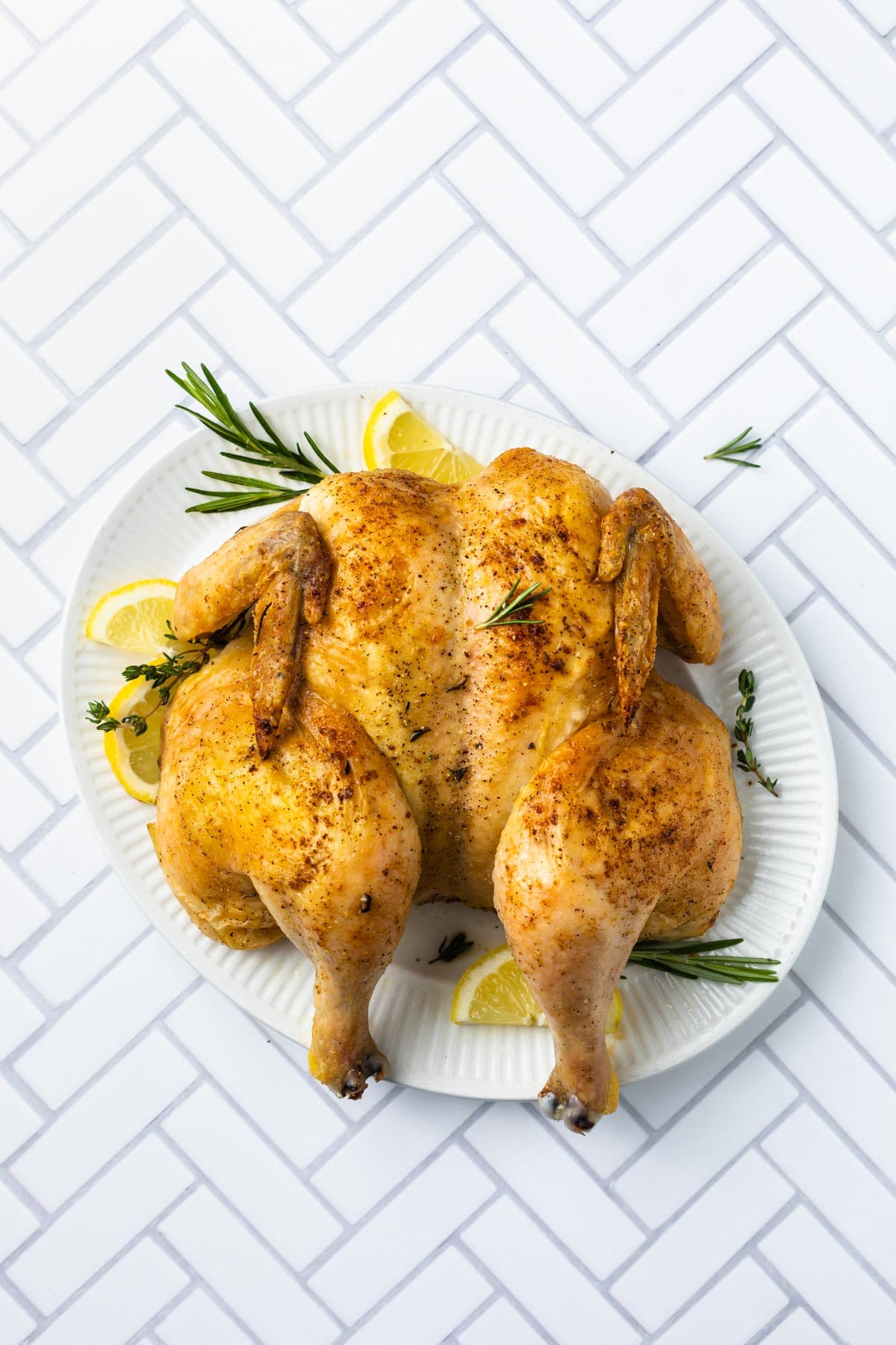 roasted chicken on a platter with fresh herbs and lemons