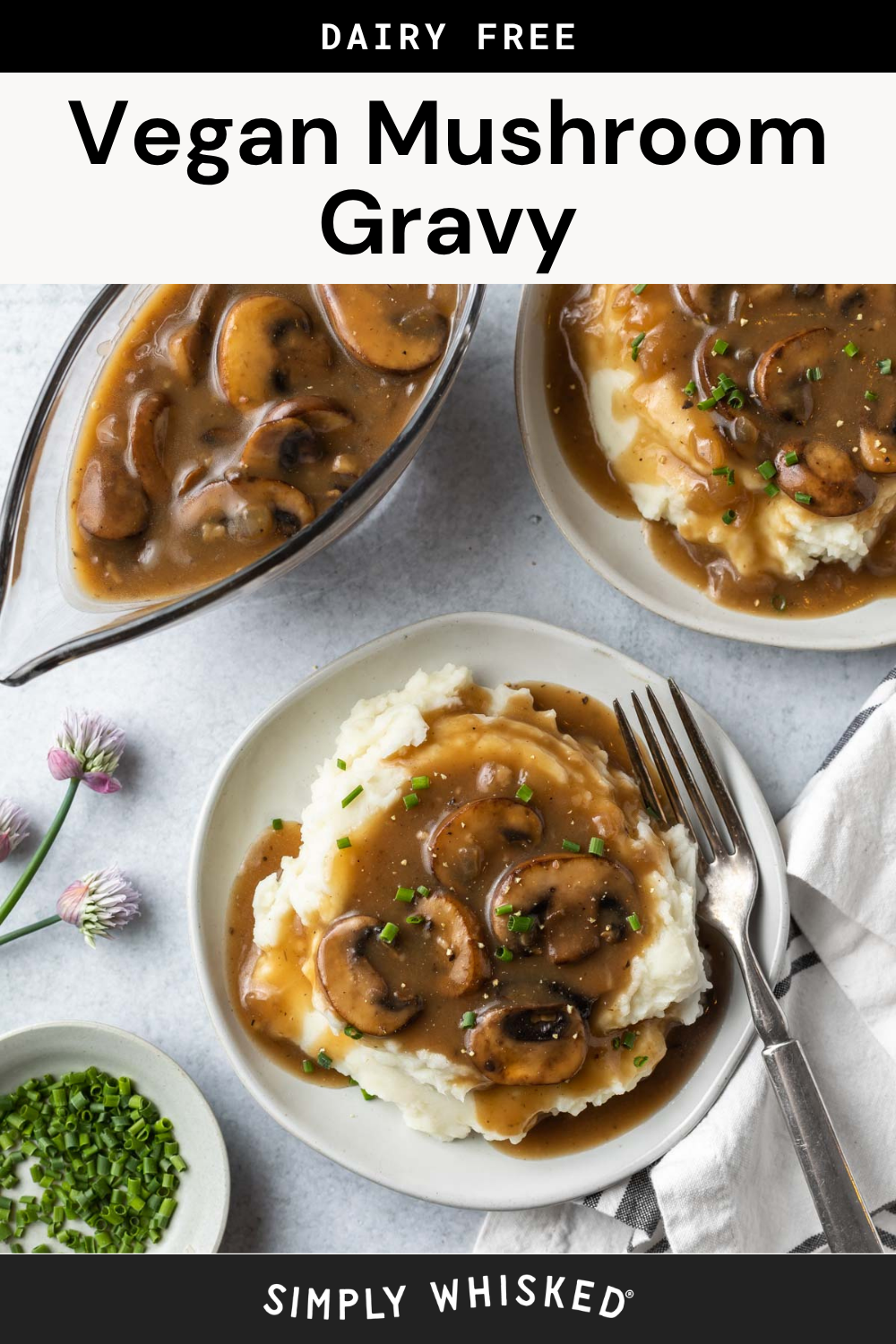 Two plates of mashed potatoes topped with rich mushroom gravy, garnished with fresh chives. A gravy boat brimming with extra mushroom gravy sits nearby, alongside a small bowl of chopped chives and a scattering of delicate purple flowers on the table.
