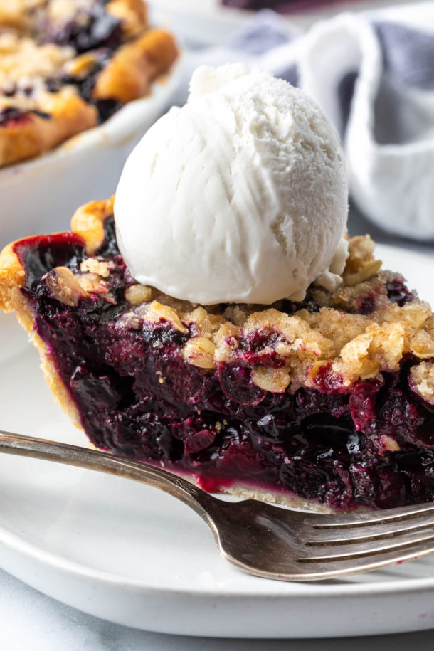 close up of side of blueberry crumble pie with a dollop of vanilla ice cream on top