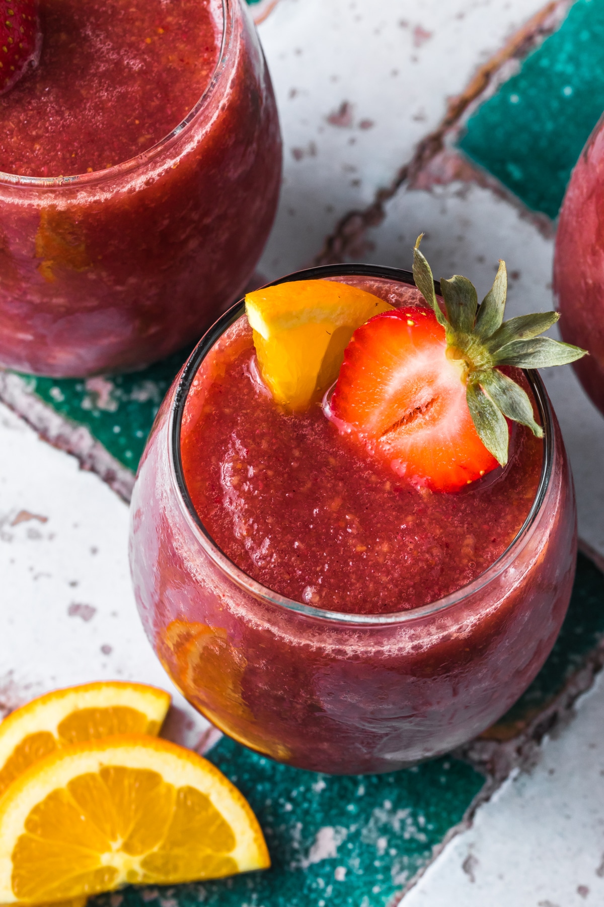 close up view of wine slushies in a glass with slice of orange and strawberry