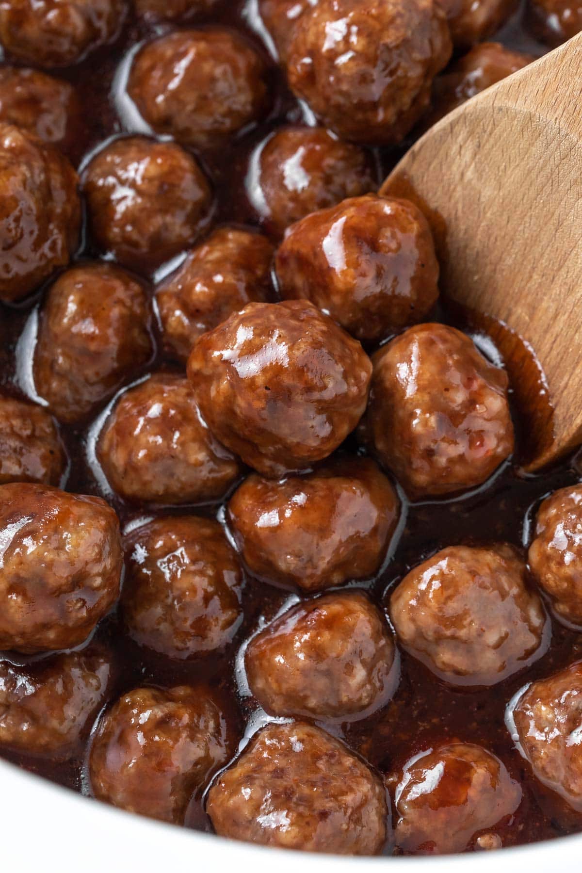 close up of slow cooker bbq meatballs with grape jelly sauce with a wooden spoon