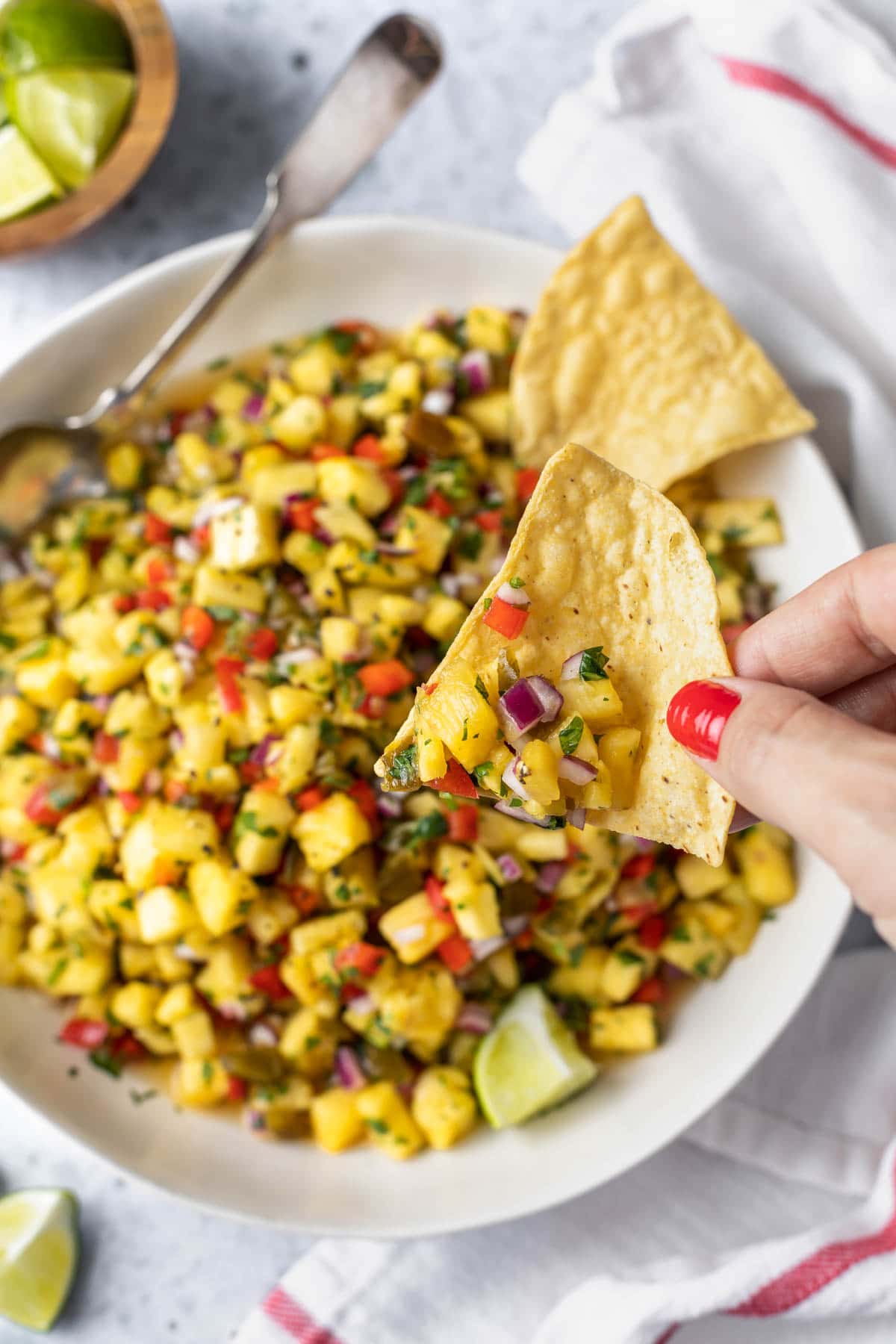overhead view of a chip with salsa being held over the serving bowl of pineapple salsa