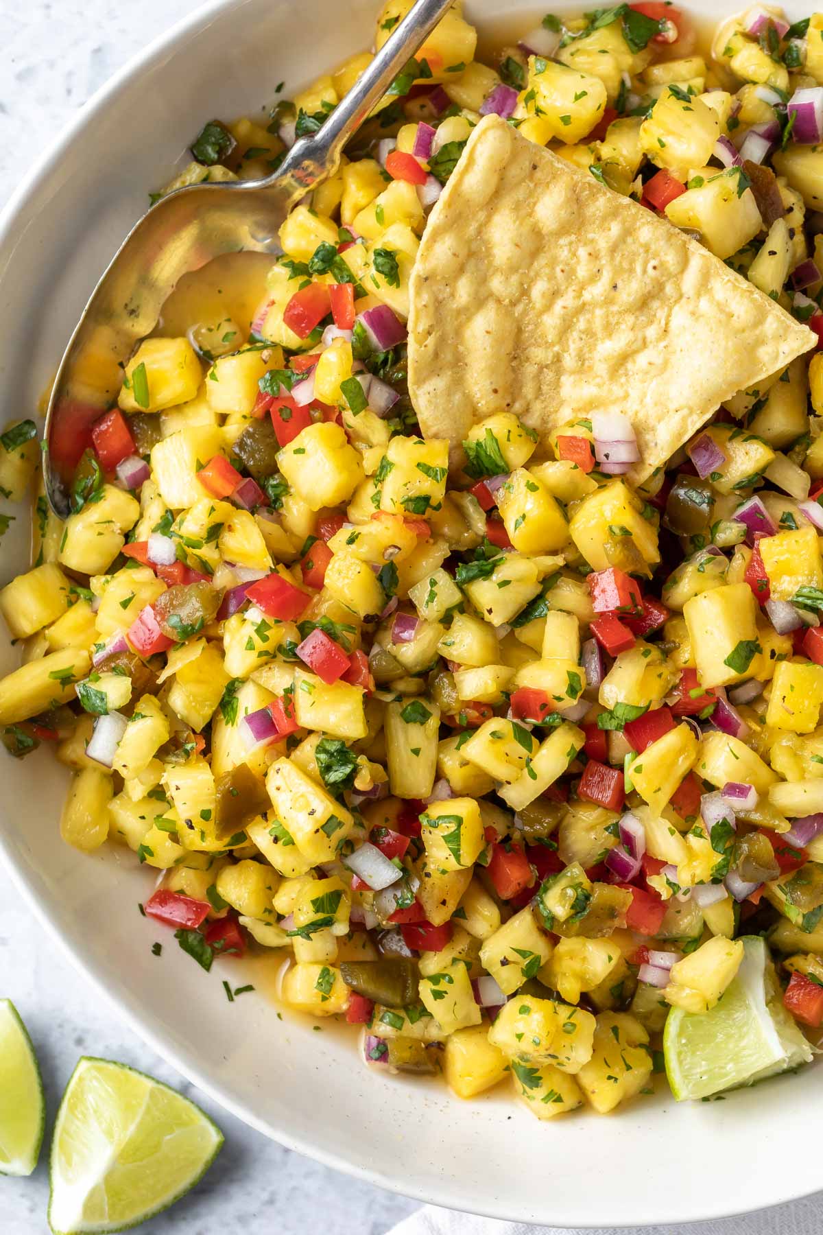 overhead close up of pineapple salsa in a white bowl with a serving spoon and a chip placed on top