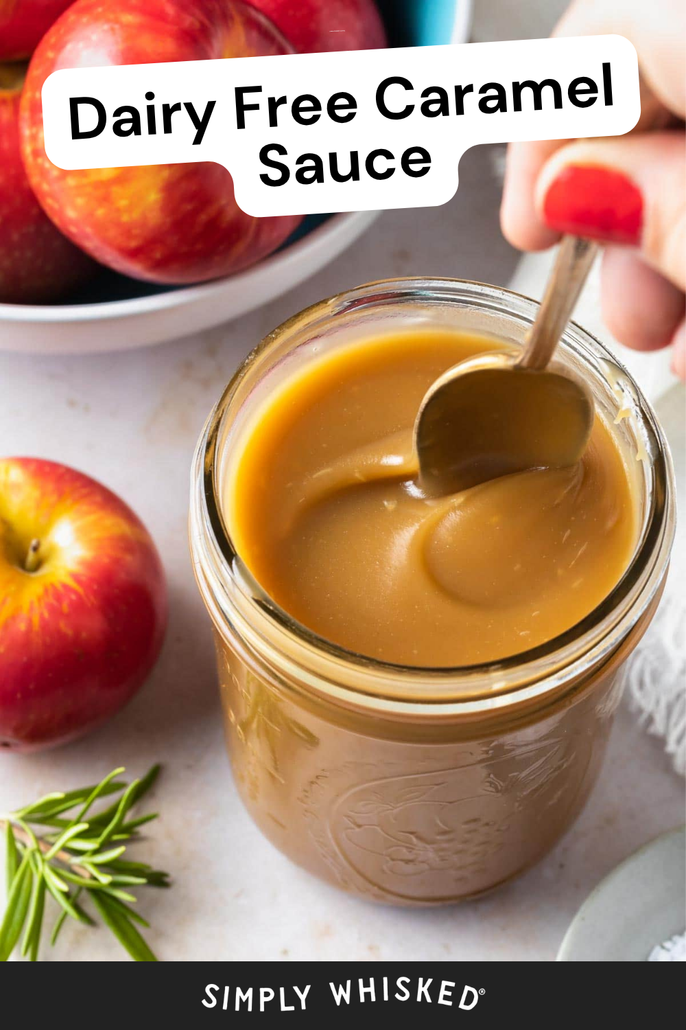 A hand stirs creamy vegan caramel sauce in a mason jar. The text reads Dairy Free Caramel Sauce. Fresh apples and a sprig of rosemary sit nearby on a light surface.