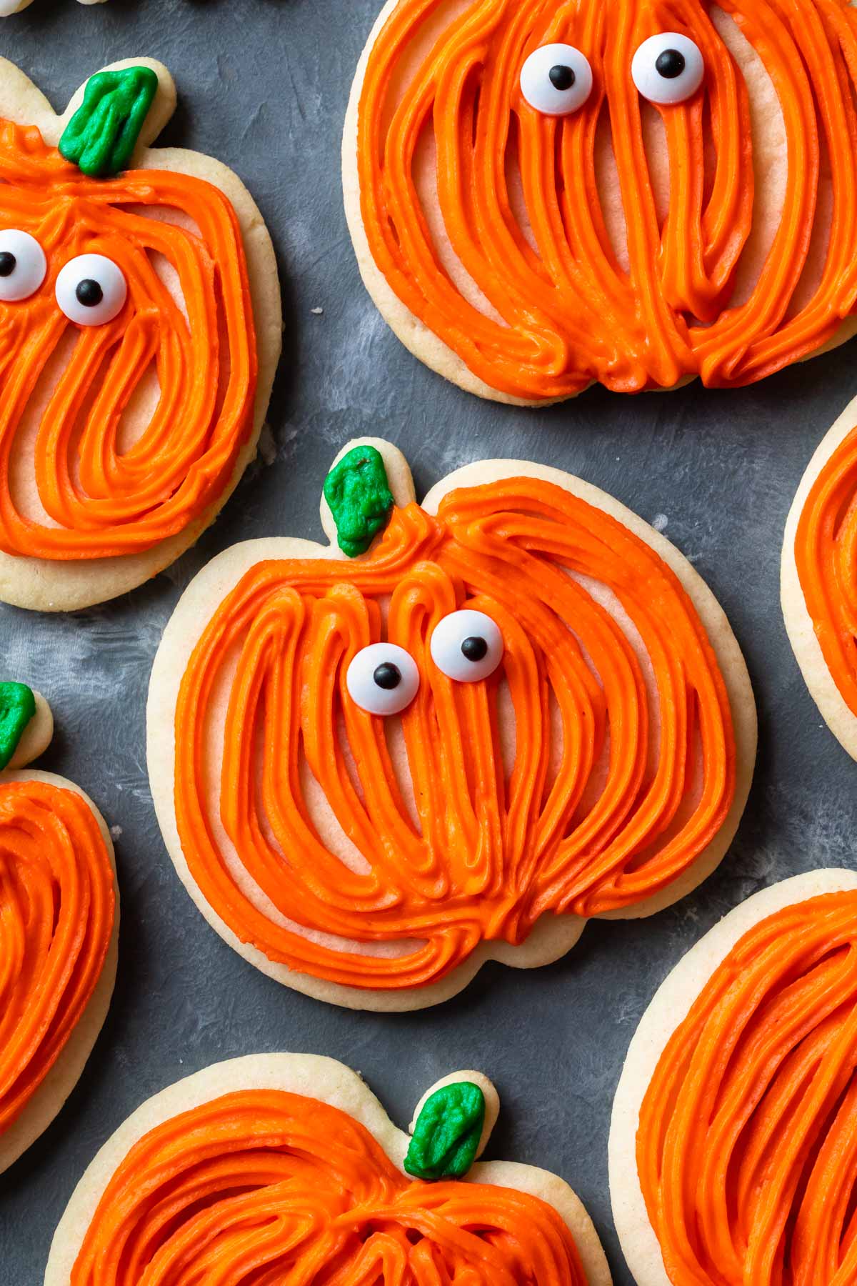 sugar cookies decorated to look like pumpkins with orange frosting and candy eyes