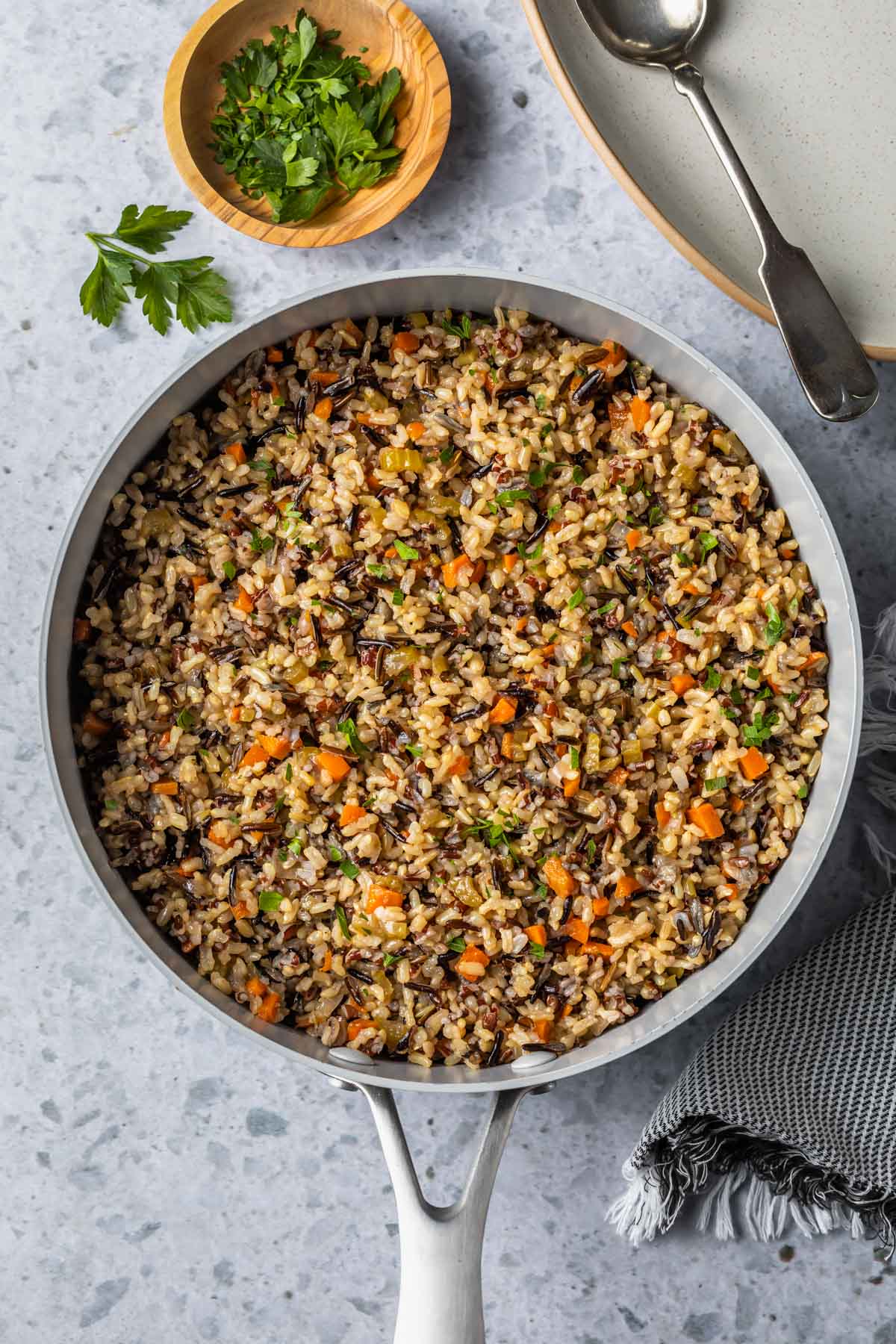overhead view of wild rice pilaf in a skillet on a countertop next to a small bowl of garnish