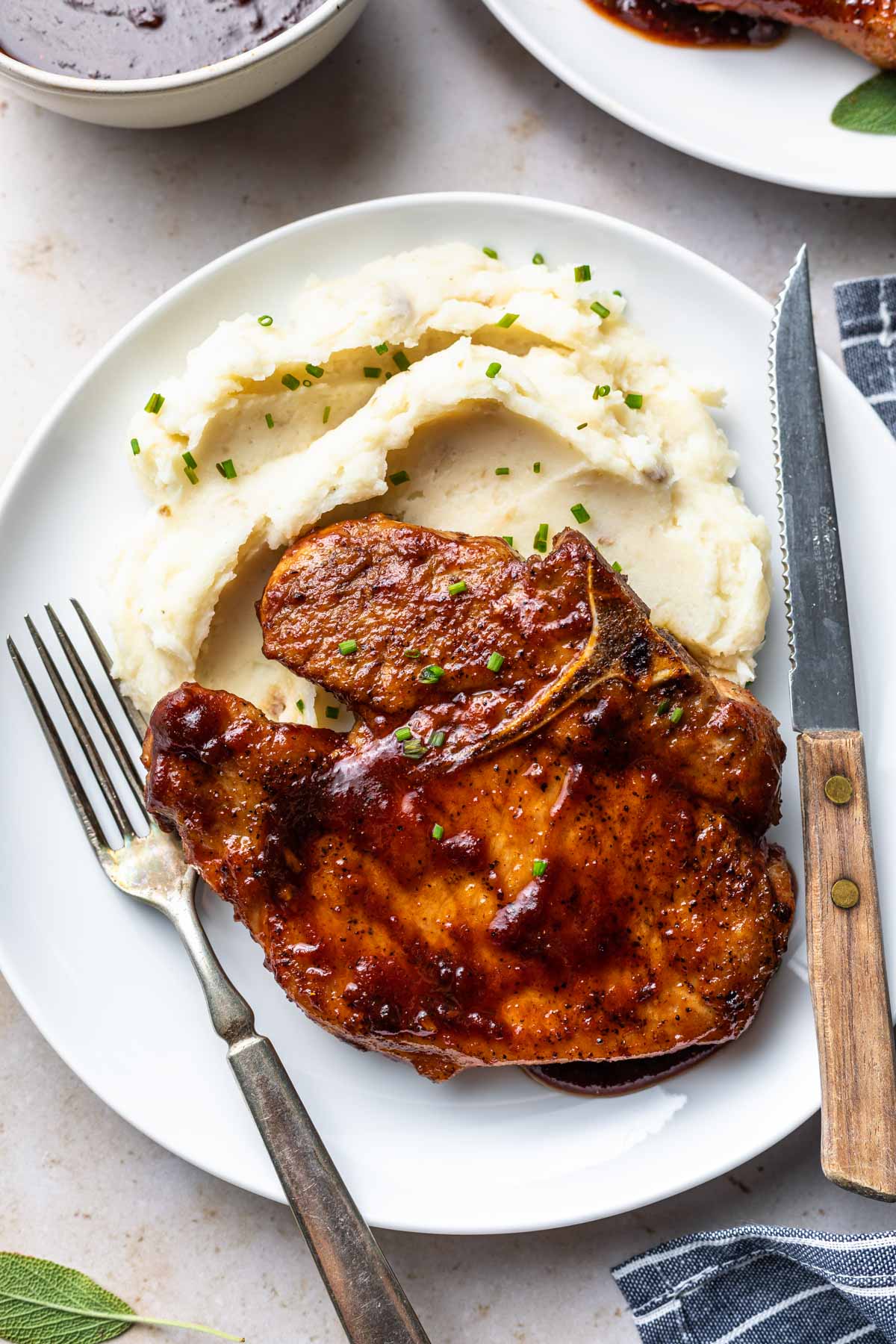 glazed pork chop on a bed of mashed potatoes with a fork and knife on a plate