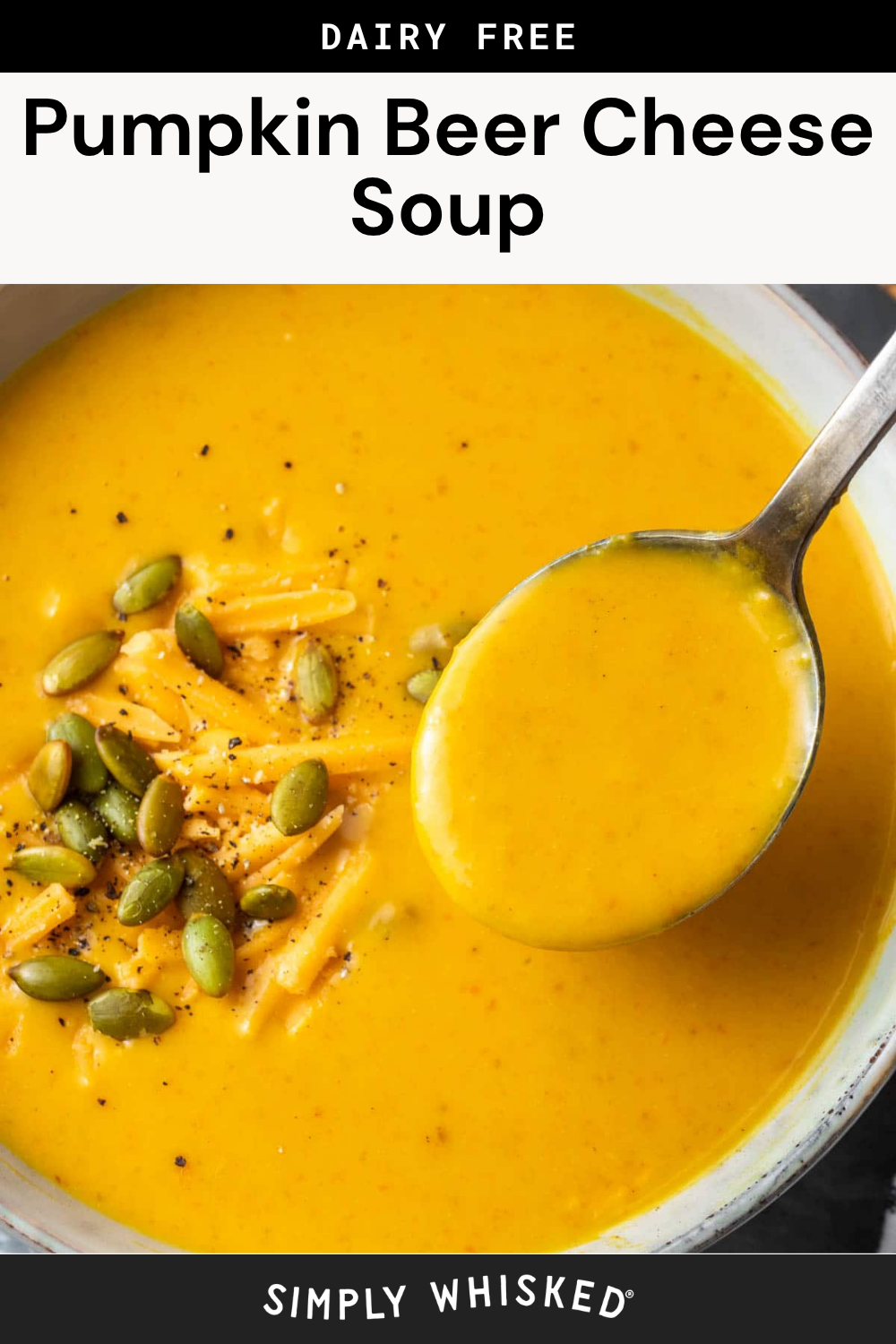 A pot of creamy orange beer cheese soup, garnished with shredded cheese, pumpkin seeds, and black pepper, with a spoon lifting some soup.