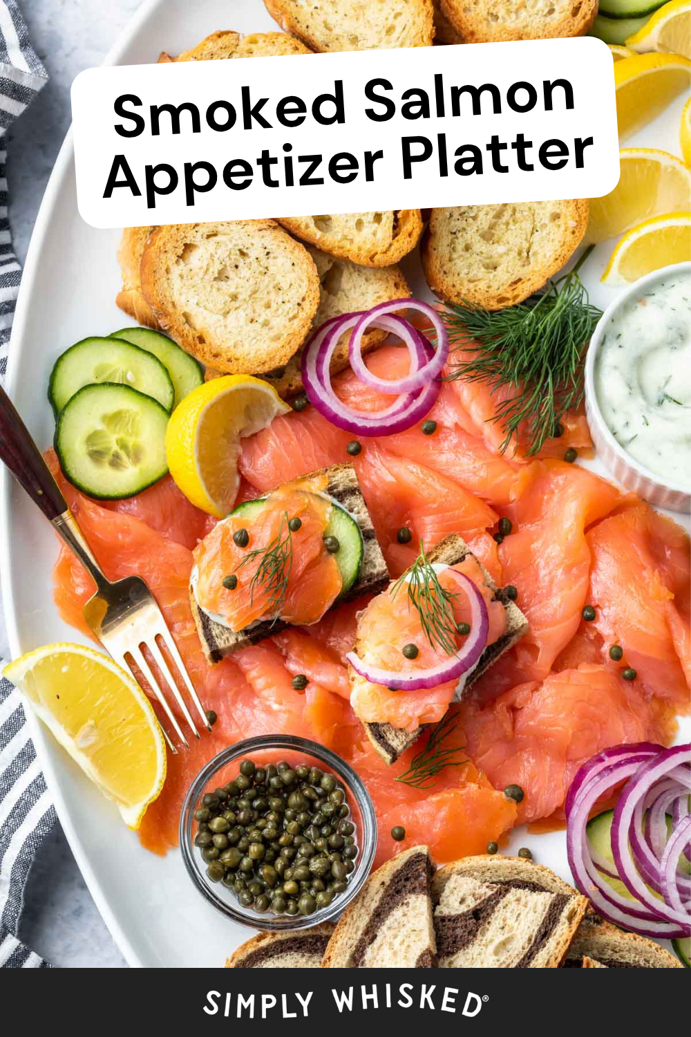 A smoked salmon appetizer platter featuring toasted bread, cucumber slices, lemon wedges, capers, dill, red onion, and a bowl of creamy dip. The text reads Smoked Salmon Appetizer Platter.