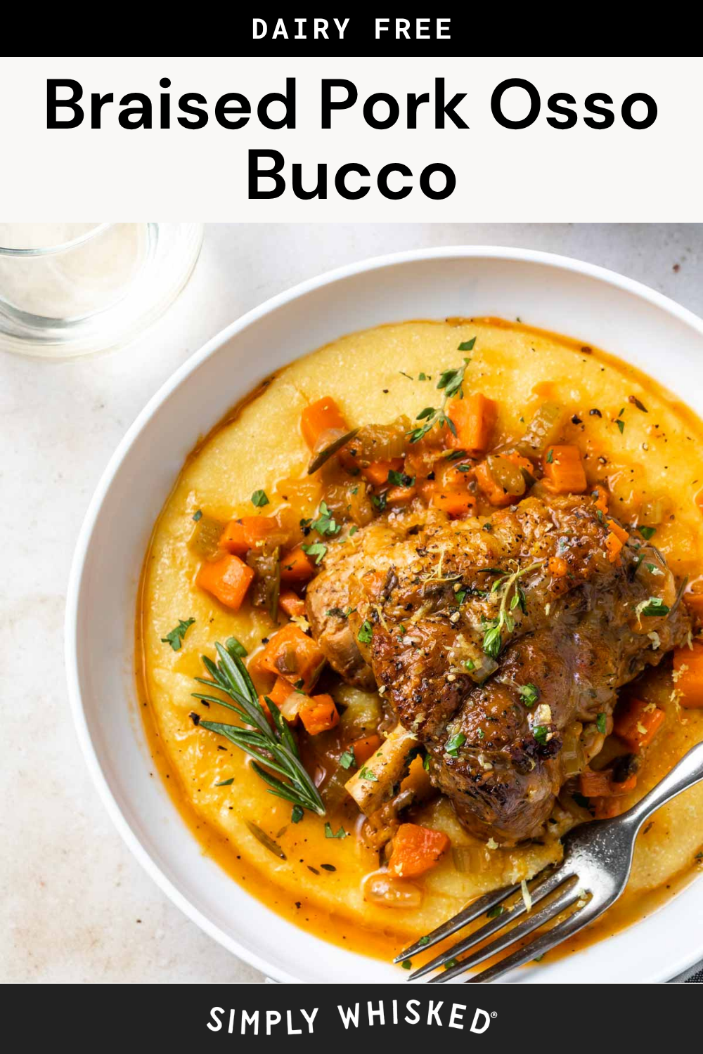 A plate of pork osso bucco, braised to tender perfection and served over creamy polenta, is topped with chopped herbs and carrots, finished with a sprig of rosemary and a fork on the side. The dish is labeled dairy free.