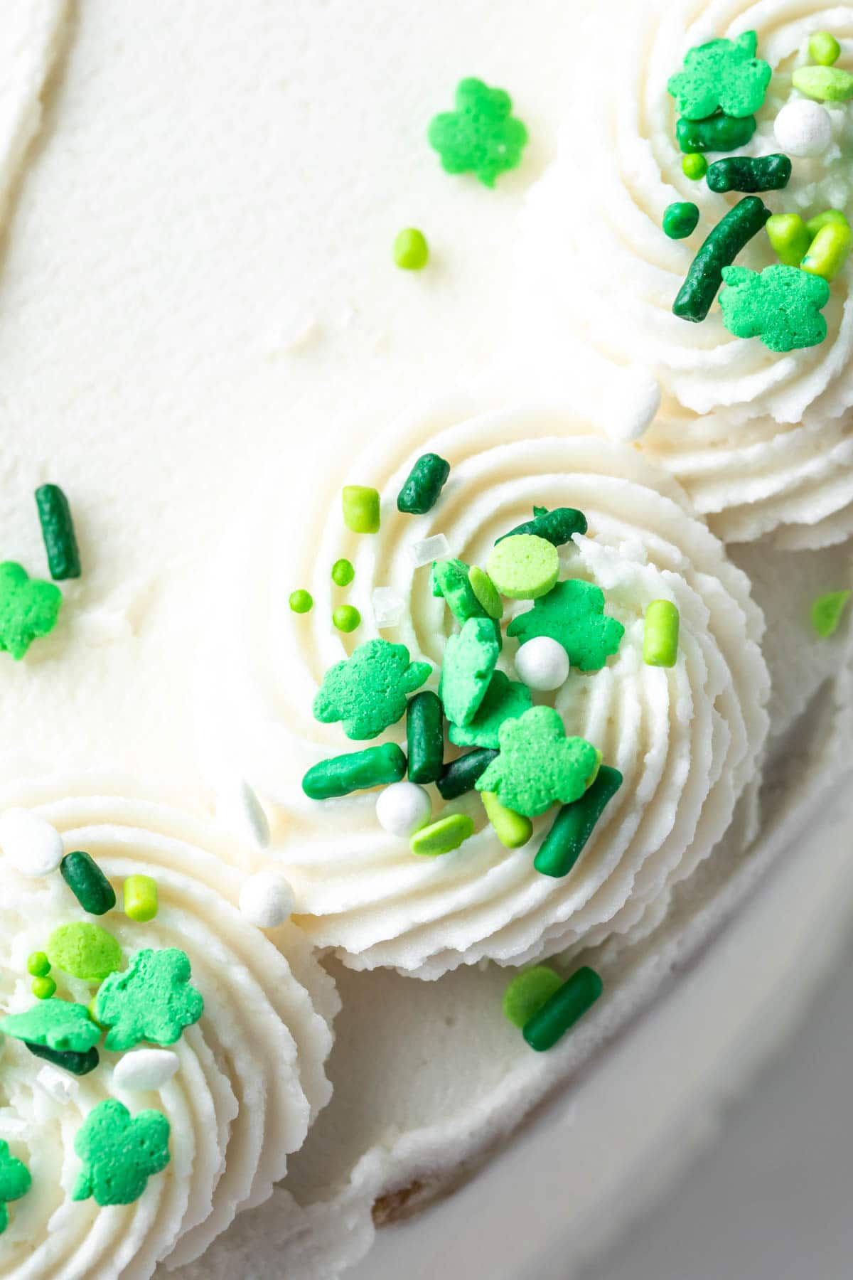 Close up of white frosting with green shamrock sprinkles. 