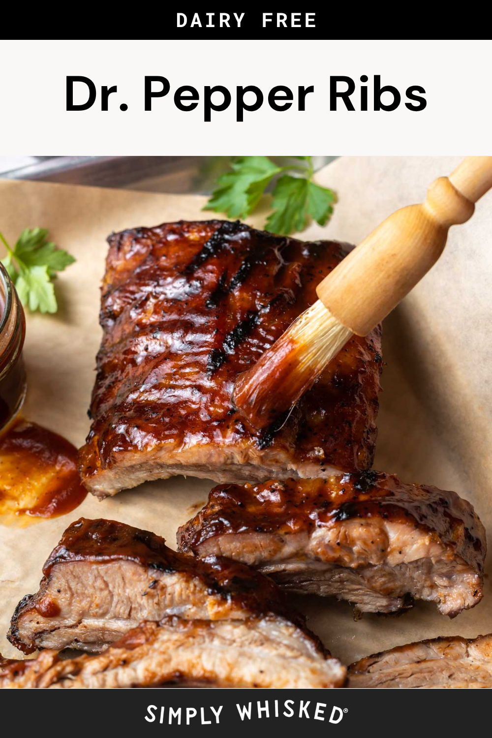 Close-up of dr. pepper ribs being brushed with sauce and garnished with herbs. The text above reads Dairy Free Dr. Pepper Ribs, while the bottom of the image says Simply Whisked.