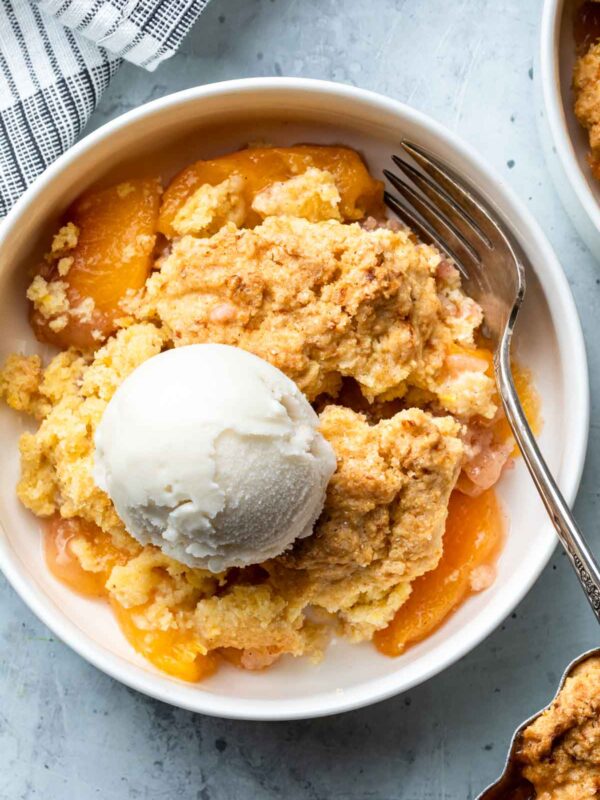 peach cobbler in a white bowl with vanilla ice cream and a fork resting in the bowl
