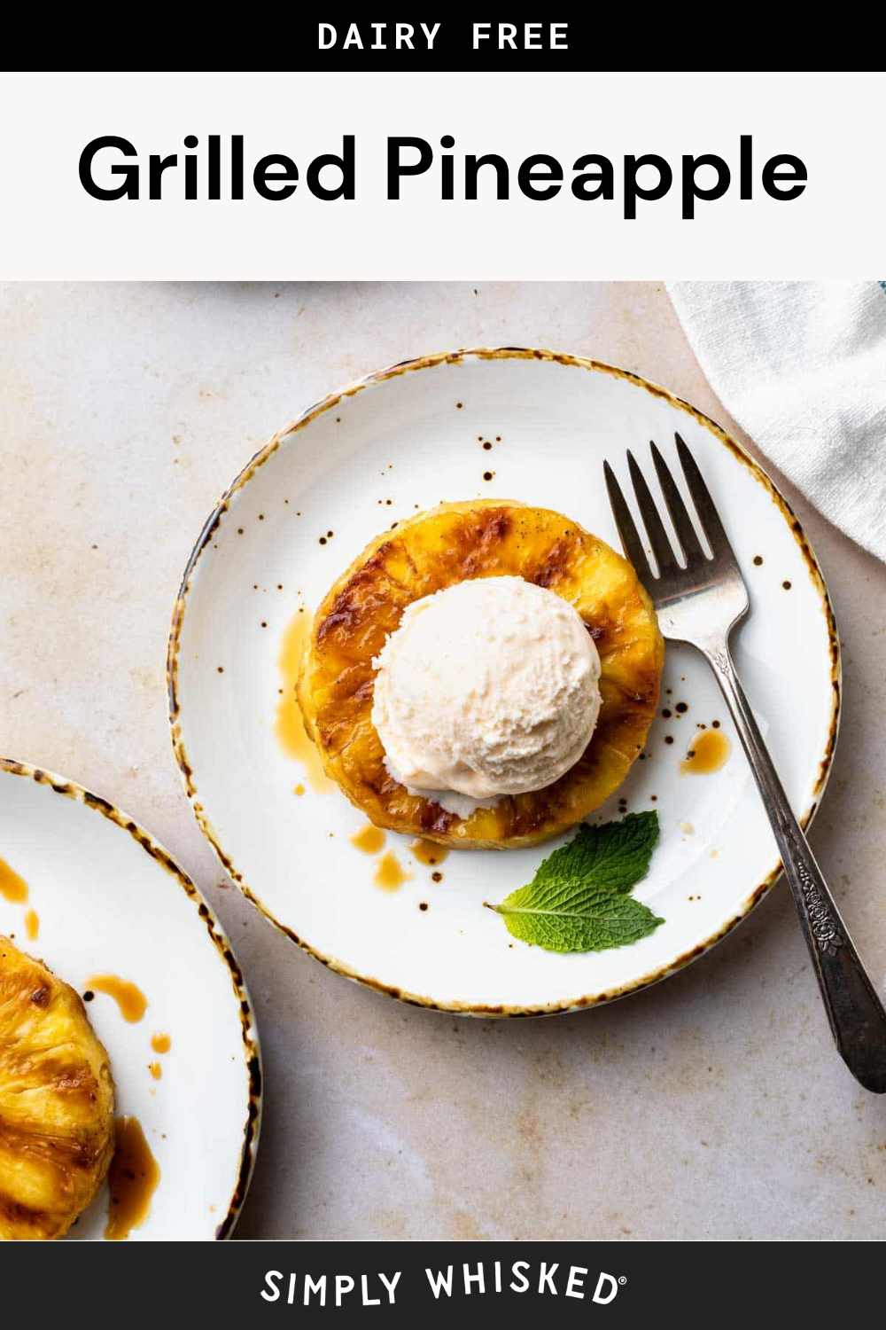 A plate with a grilled pineapple slice topped with a scoop of ice cream, garnished with mint. A fork rests on the plate; a second plate is partially visible. Text above reads Dairy Free Grilled Pineapple, showcasing the delicious simplicity of this grilled pineapple dessert.