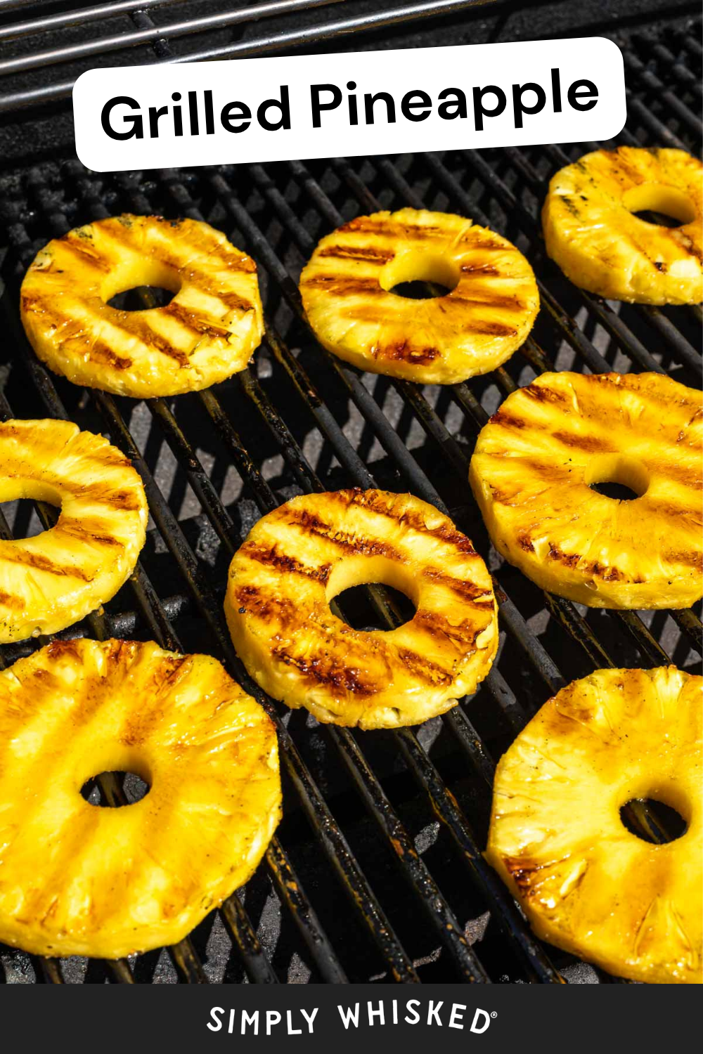 Sliced grilled pineapple rings with charred grill marks are cooking on a grill. The text Grilled Pineapple appears at the top, and Simply Whisked is written at the bottom.