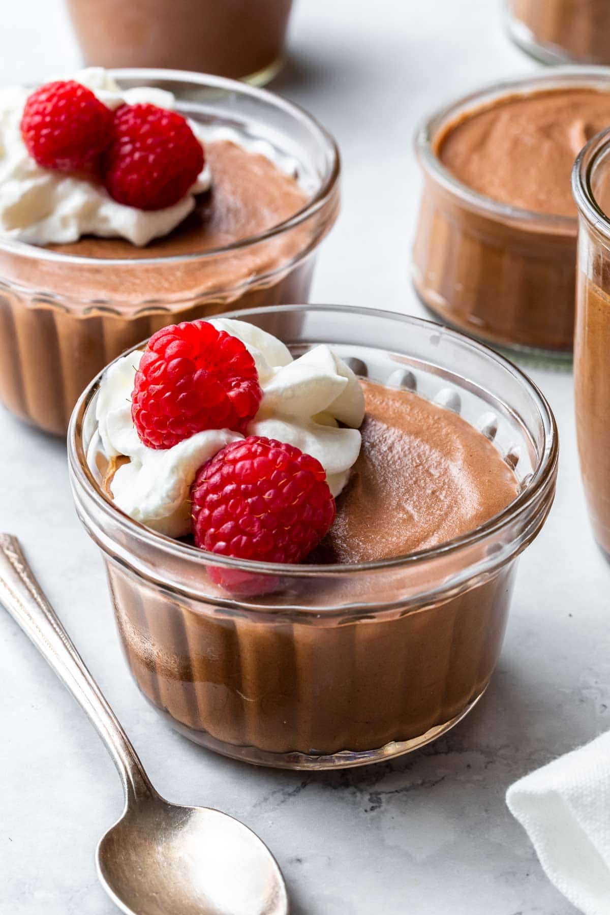 2 small glass bowls of chocolate mousse with a dollop of whipped cream and raspberries.