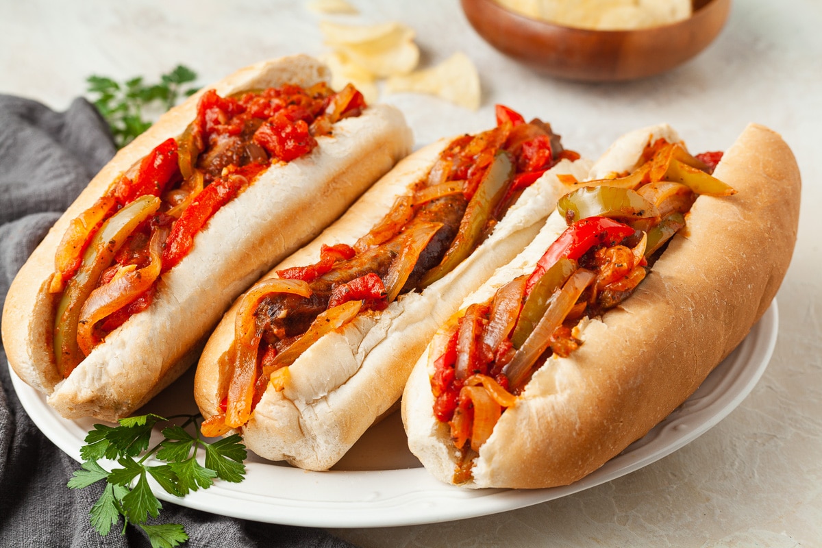 3 sausage, red pepper, and onion sandwiches on a plate with some parsley garnishing the plate. 