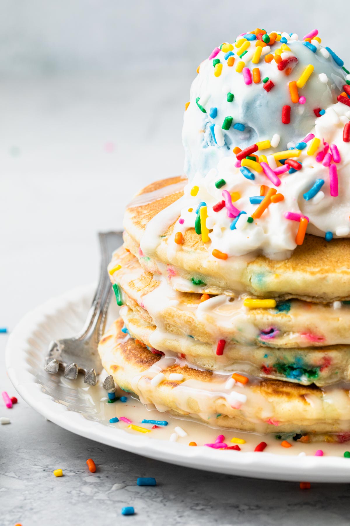 A stack of funfetti pancakes topped with whipped cream, blue birthday cake ice cream, and rainbow sprinkles.