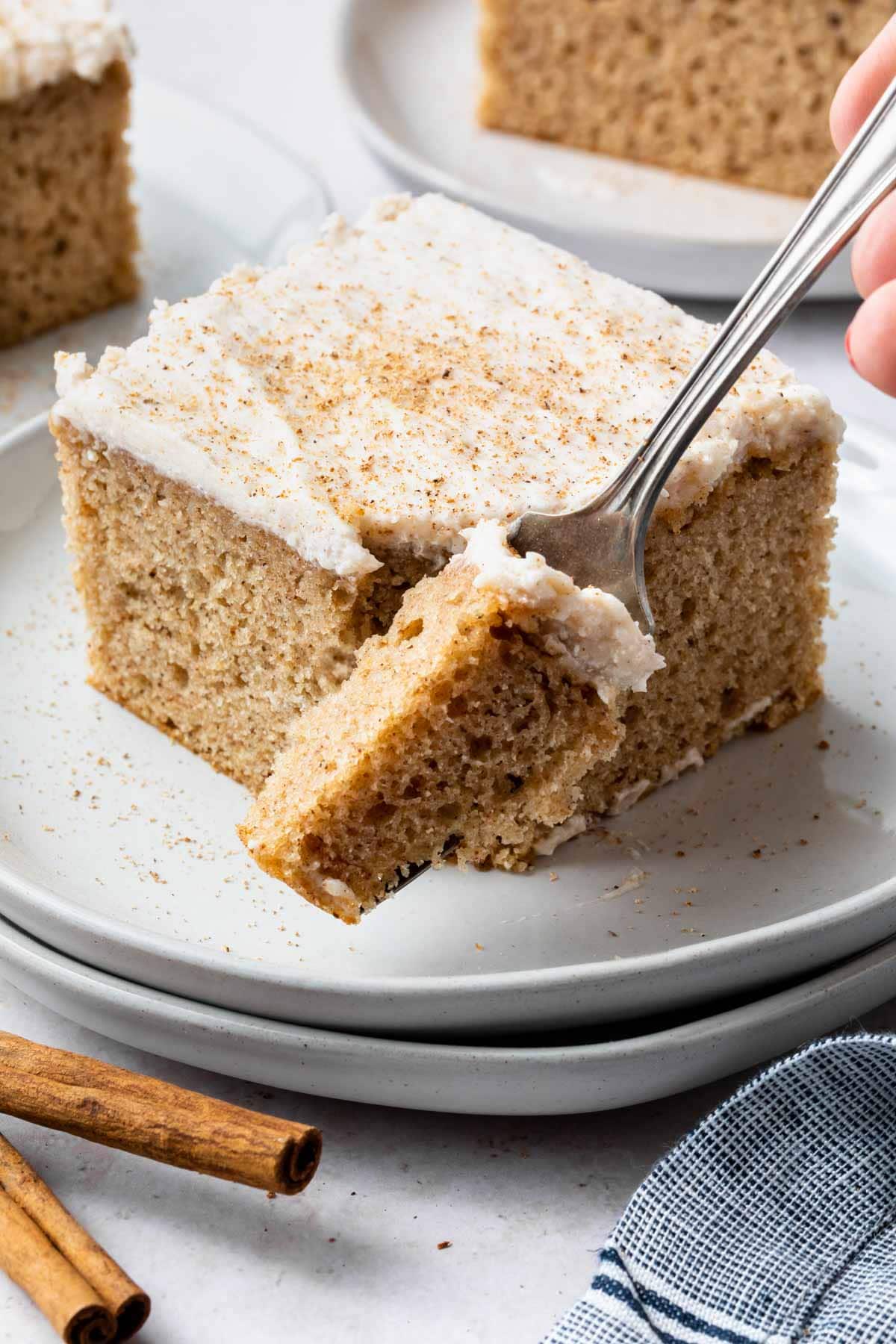 A square of chai spice cake on a white plate with a corner removed on a fork. 