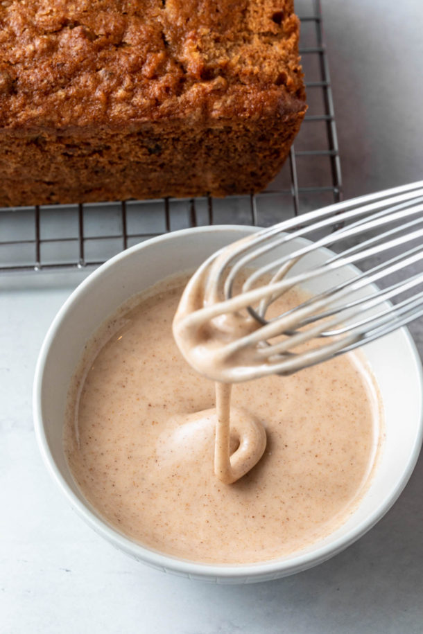 A whisk with cinnamon glazed drizzling from it into a bowl. 