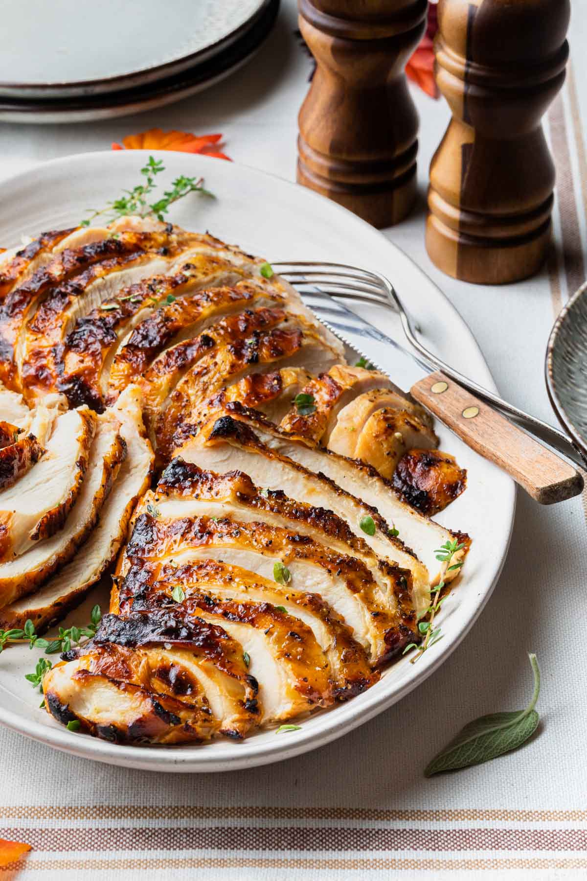 Grilled turkey breast on a platter sliced and ready to serve, a fork and knife resting on the platter.
