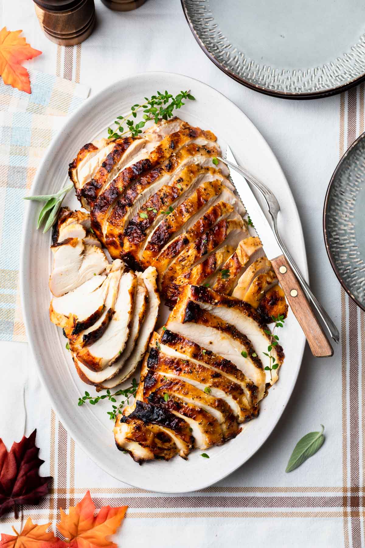 Overhead shot of grilled turkey breast on a platter sliced and ready to serve, with a fork and knife resting on the platter