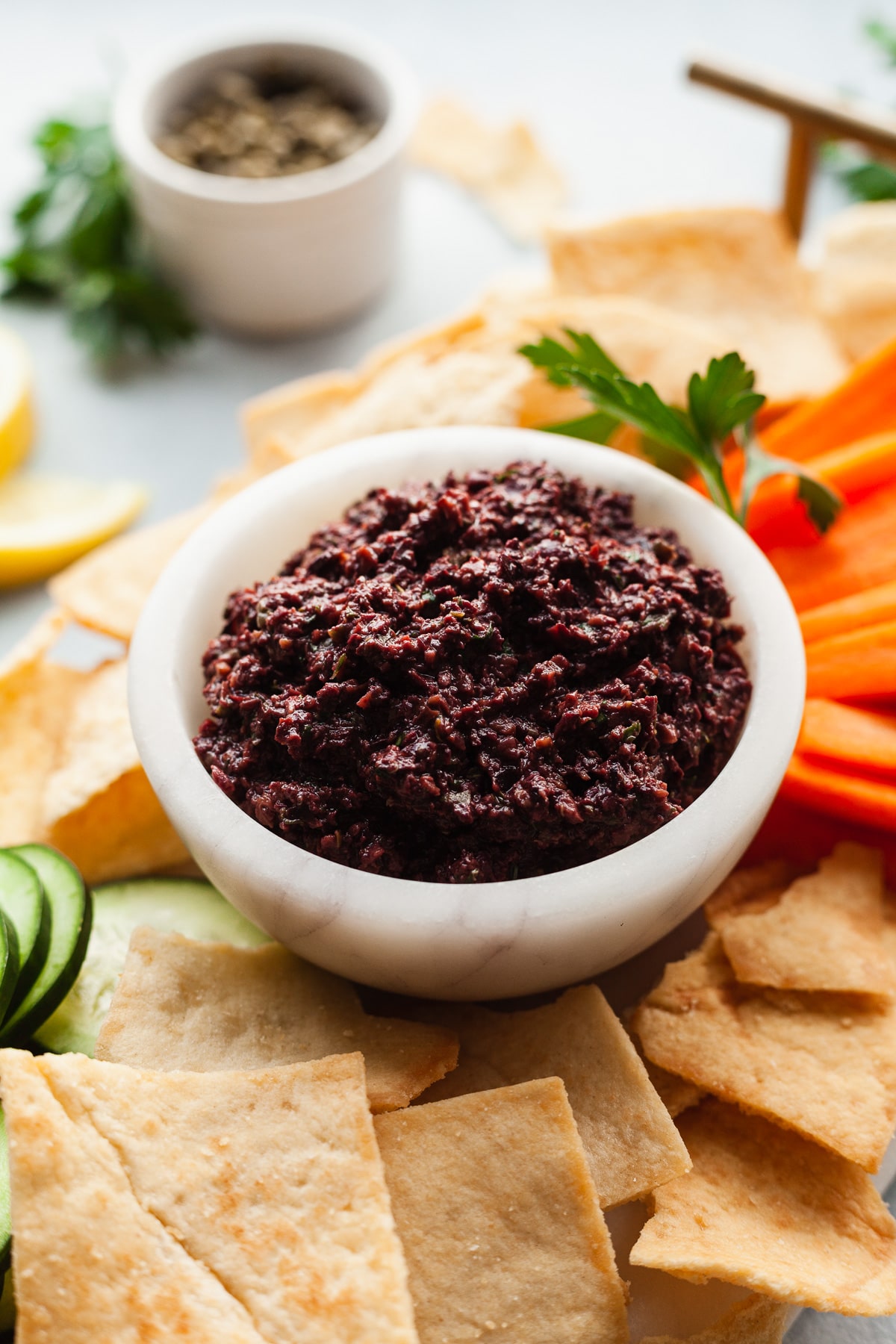 Close up of olive tapenade in a small bowl with pita chips and fresh veggies. 