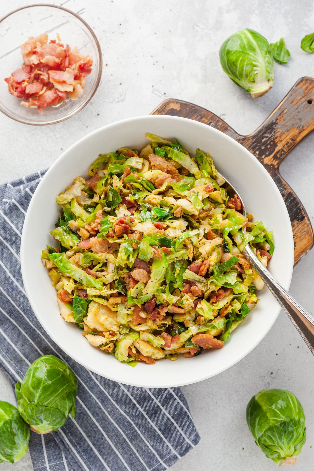 A bowl of sauteed brussels sprouts with bacon, in a white bowl with a fork in it. 