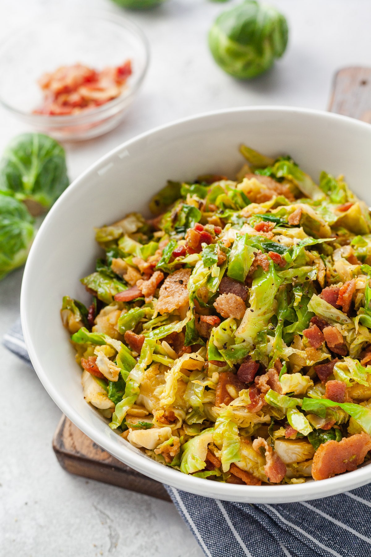 A close up of a bowl of sauteed brussels sprouts with bacon in a white bowl.