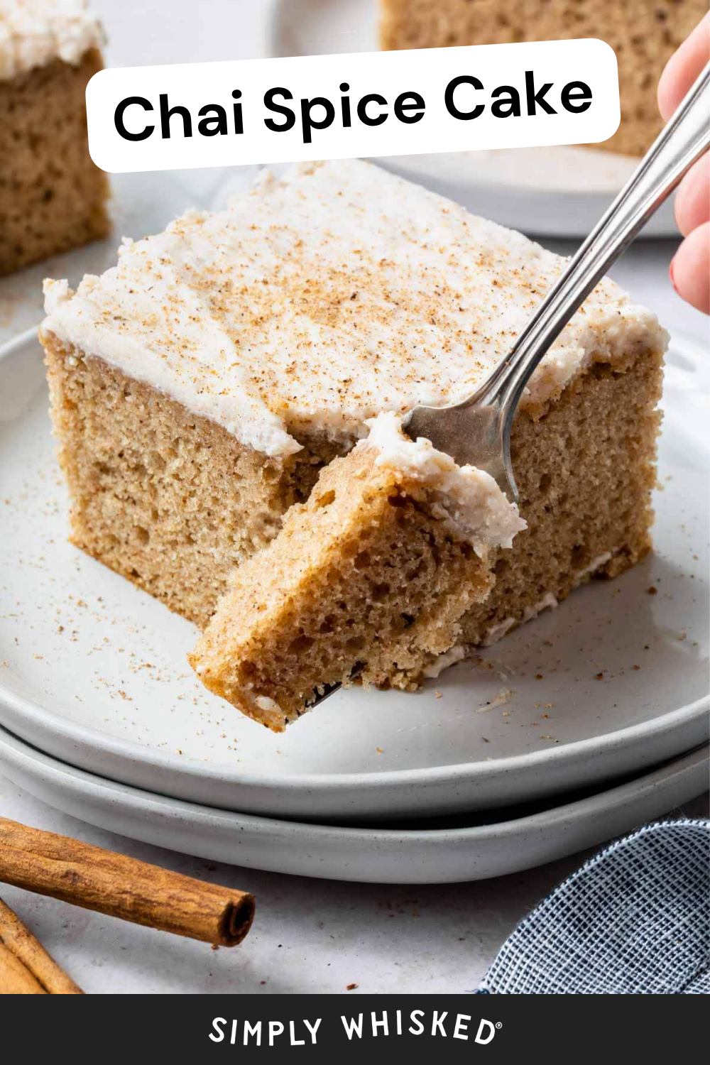 A slice of spice cake with white frosting sits on a plate, topped with sprinkled spices. A fork is cutting a piece. A cinnamon stick lies nearby. The words Chai Spice Cake and Simply Whisked appear on the image.
