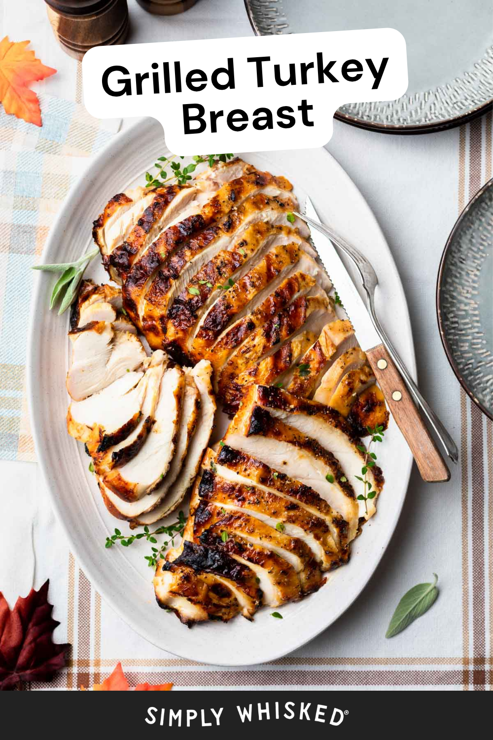 Sliced grilled turkey breast arranged on a white oval plate, garnished with herbs. A carving knife and fork are beside the tender turkey breast, with plates and autumn-themed decorations nearby.