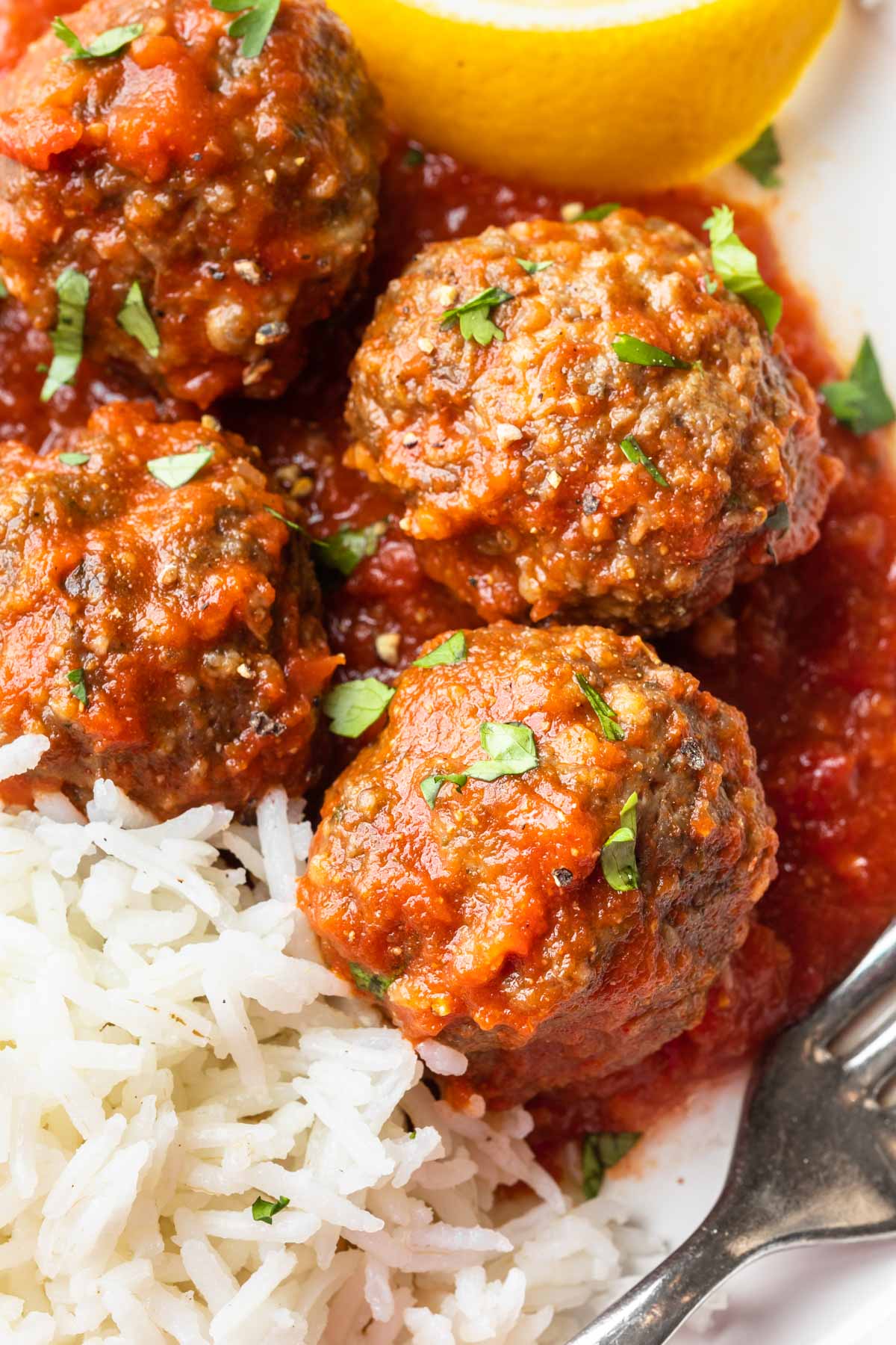 Close up of Moroccan meatballs and white rice, garnished with chopped fresh parsley. 