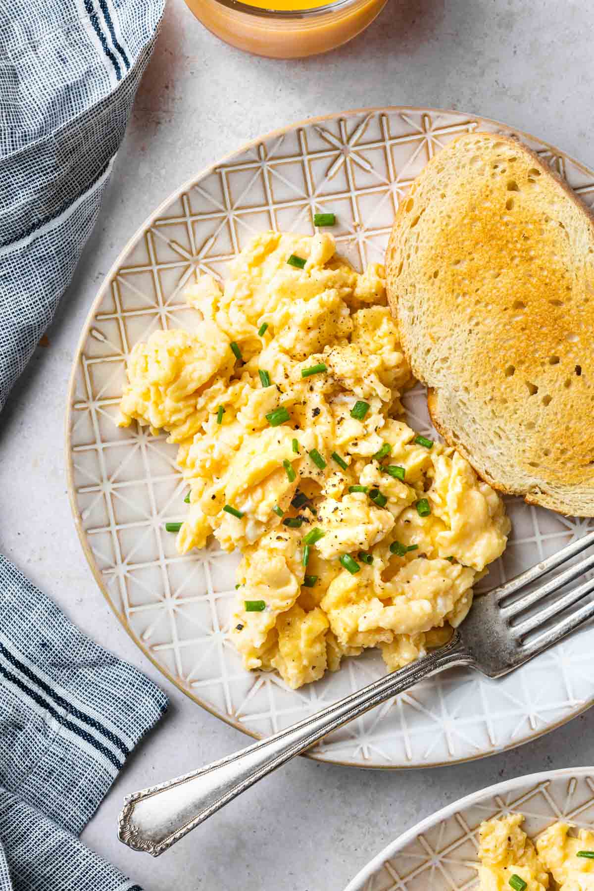 Scrambled eggs sprinkled with chives and salt and pepper on a plate with some toast and a fork. 