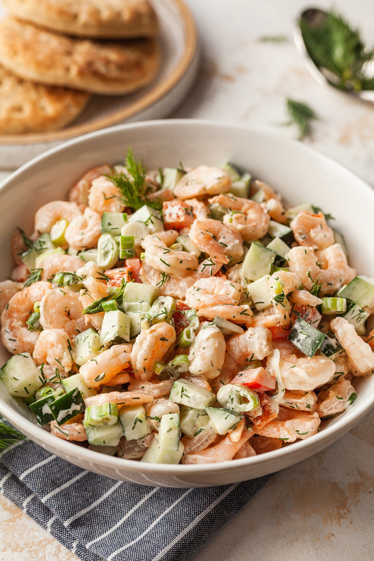 Shrimp salad in a serving bowl with a plate of pita bread in the background. 