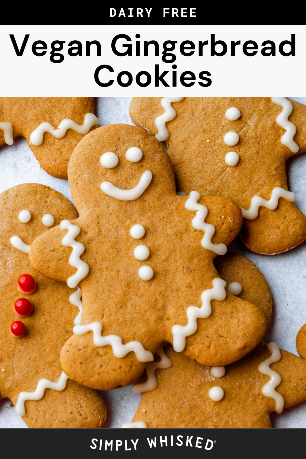 Vegan gingerbread cookies shaped like people are decorated with white icing and some with red candies, all arranged on a white surface. The text “Dairy Free Vegan Gingerbread Cookies” appears at the top, highlighting these festive and delicious vegan gingerbread cookies.