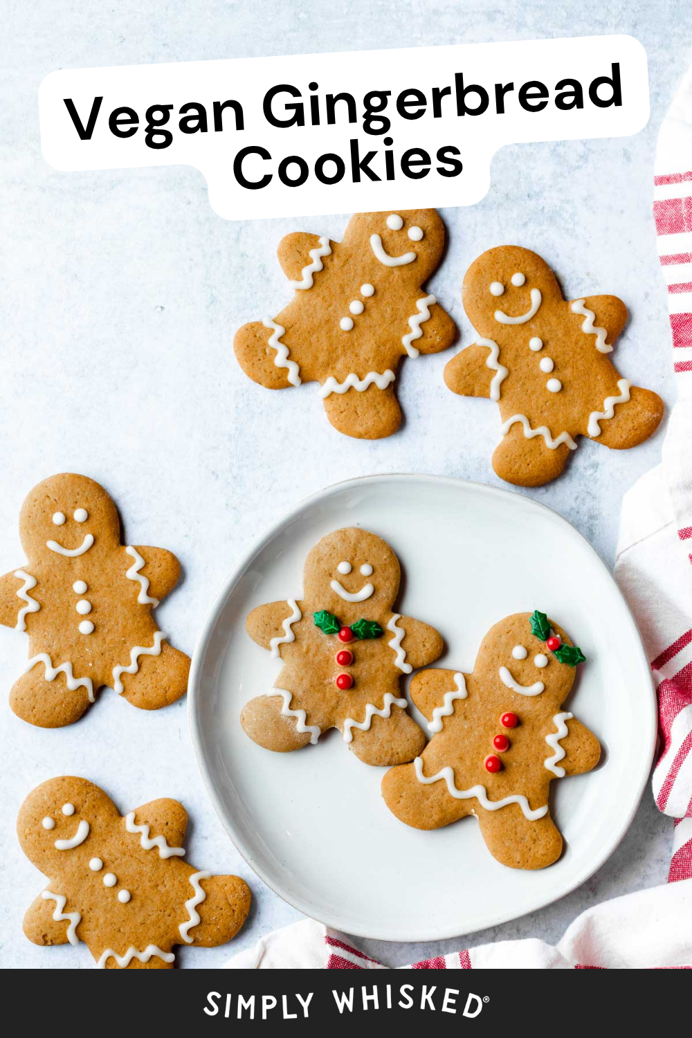 Five vegan gingerbread cookies with white icing details are arranged on a light surface, with two decorated cookies placed on a round white plate. A red and white cloth is partially visible on the right. Text above reads, Vegan Gingerbread Cookies.
