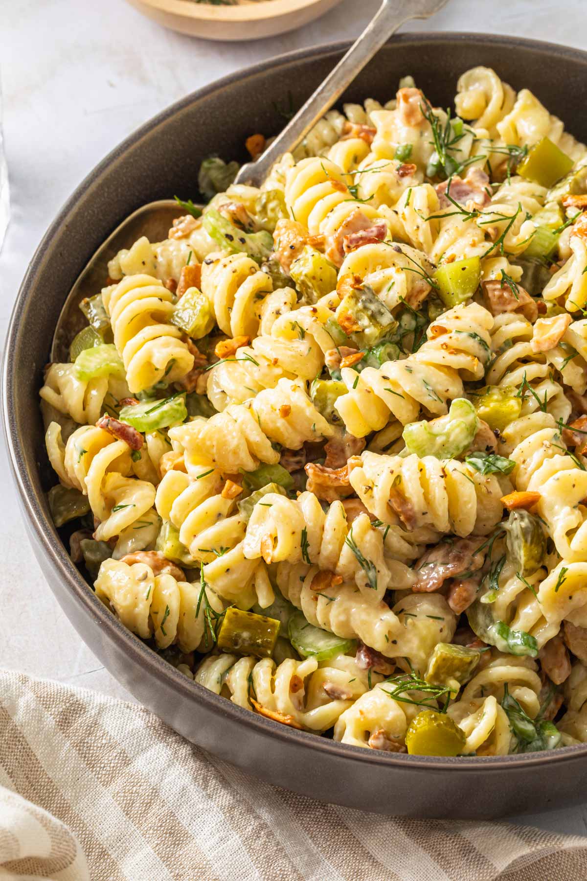 A serving bowl of dill pickle pasta salad garnished with chopped fresh dill. 
