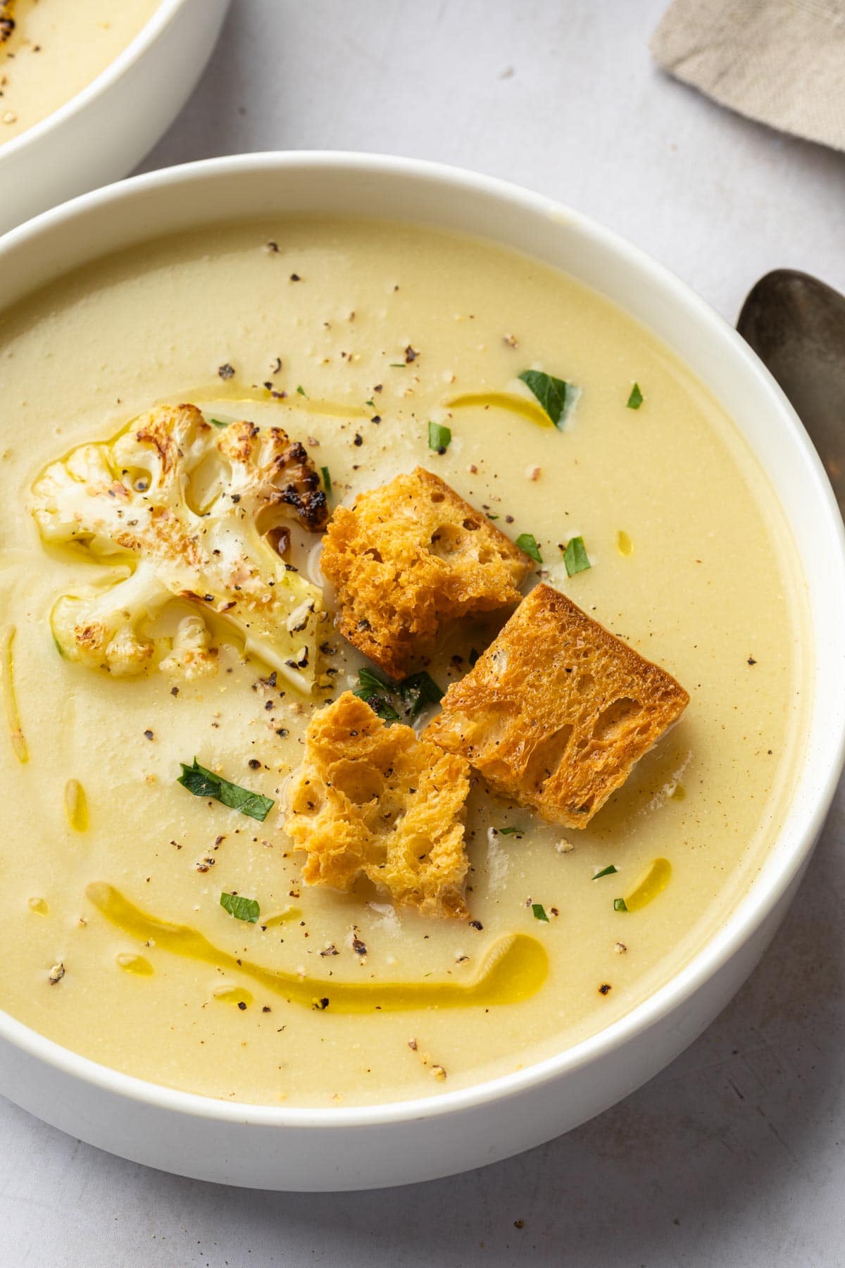 Close up of a bowl of cauliflower soup topped with croutons and a piece of roasted cauliflower. 
