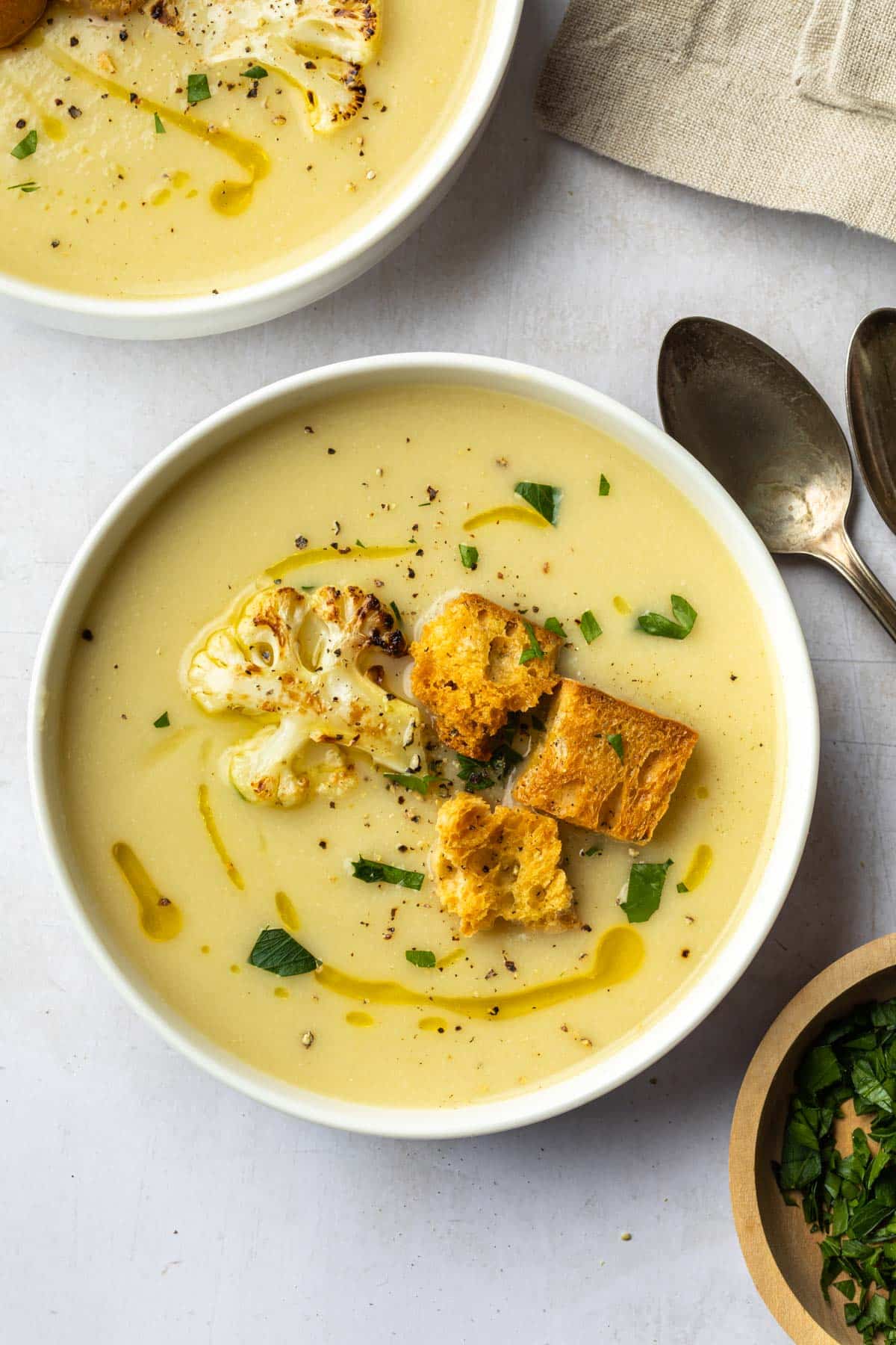 2 bowls of cauliflower soup topped with toasted croutons and a piece of roasted cauliflower. 
