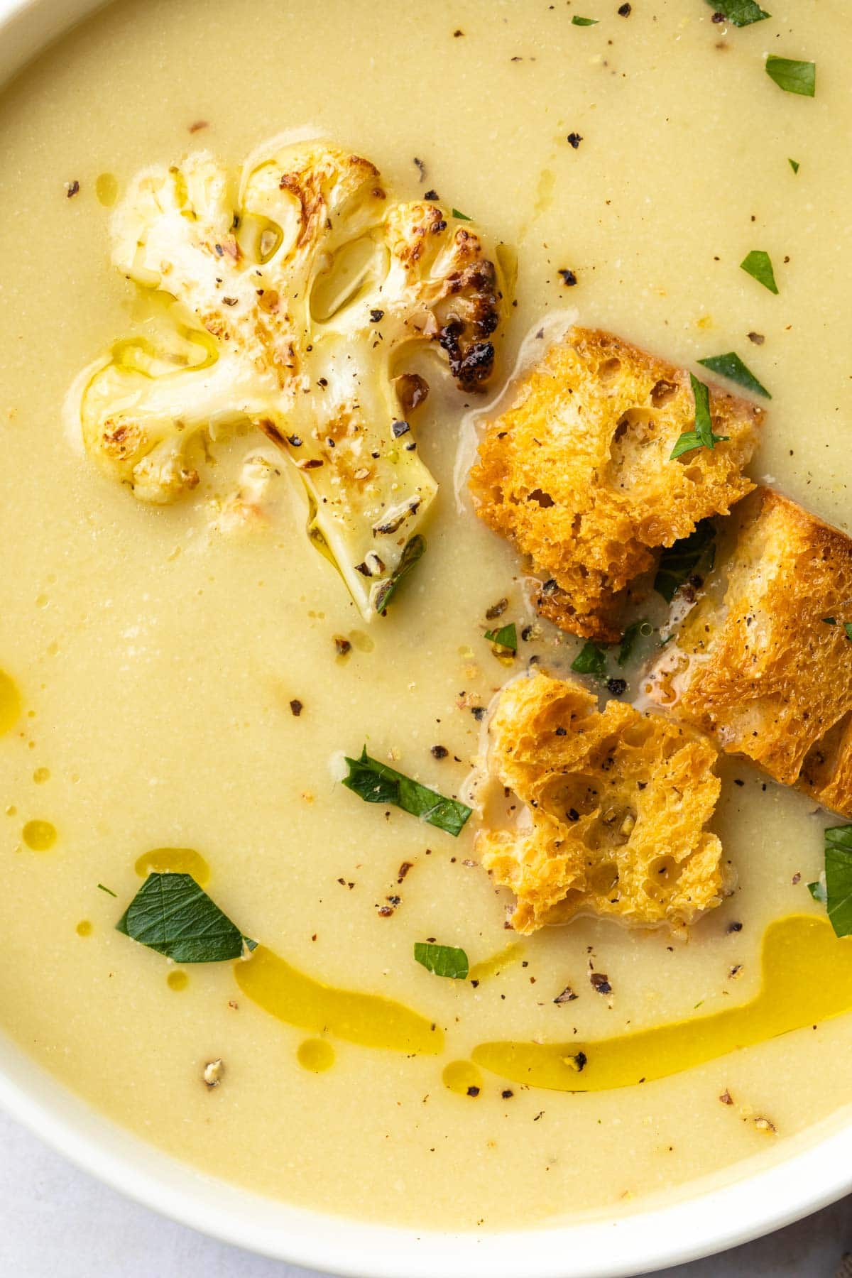 Close up of a bowl of cauliflower soup topped with croutons and roasted cauliflower. 