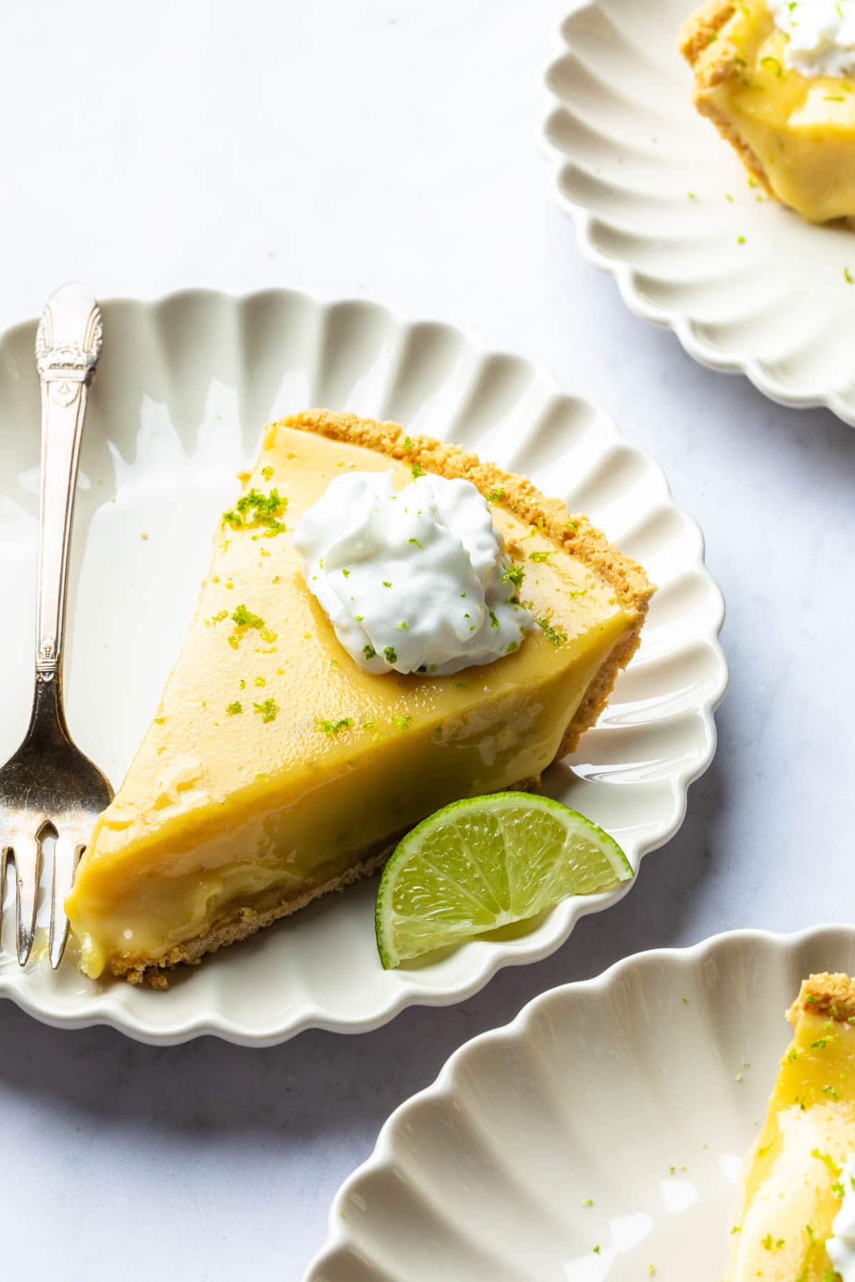 Slices of dairy free key lime pie on plates topped with whipped cream and lime zest. 