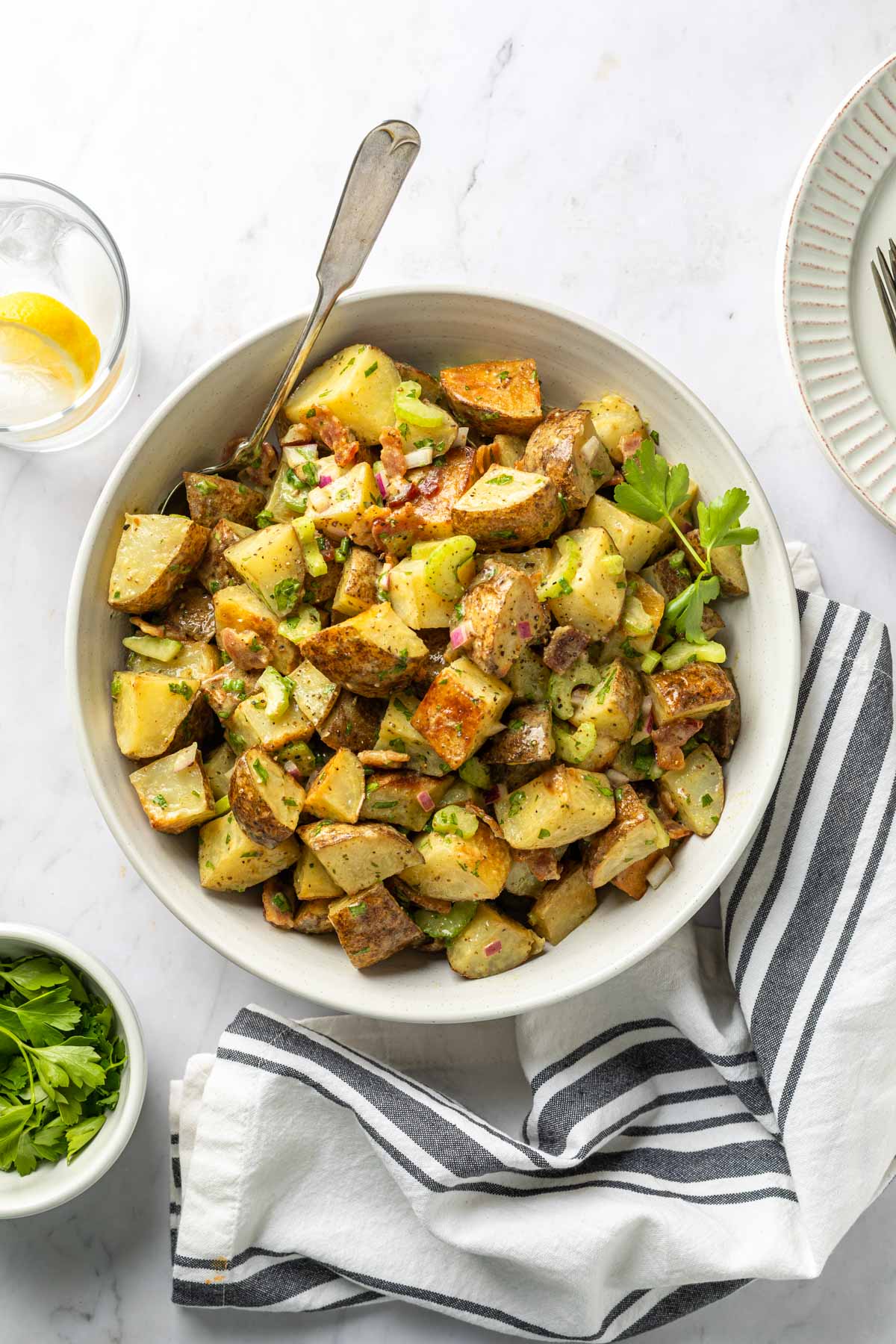 A serving bowl of roasted german potato salad garnished parsley. 