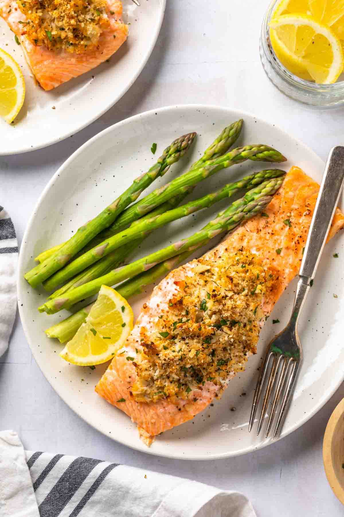 A salmon fillet stuffed with crab meat on a plate with a serving of asparagus, a lemon wedge and a fork. 