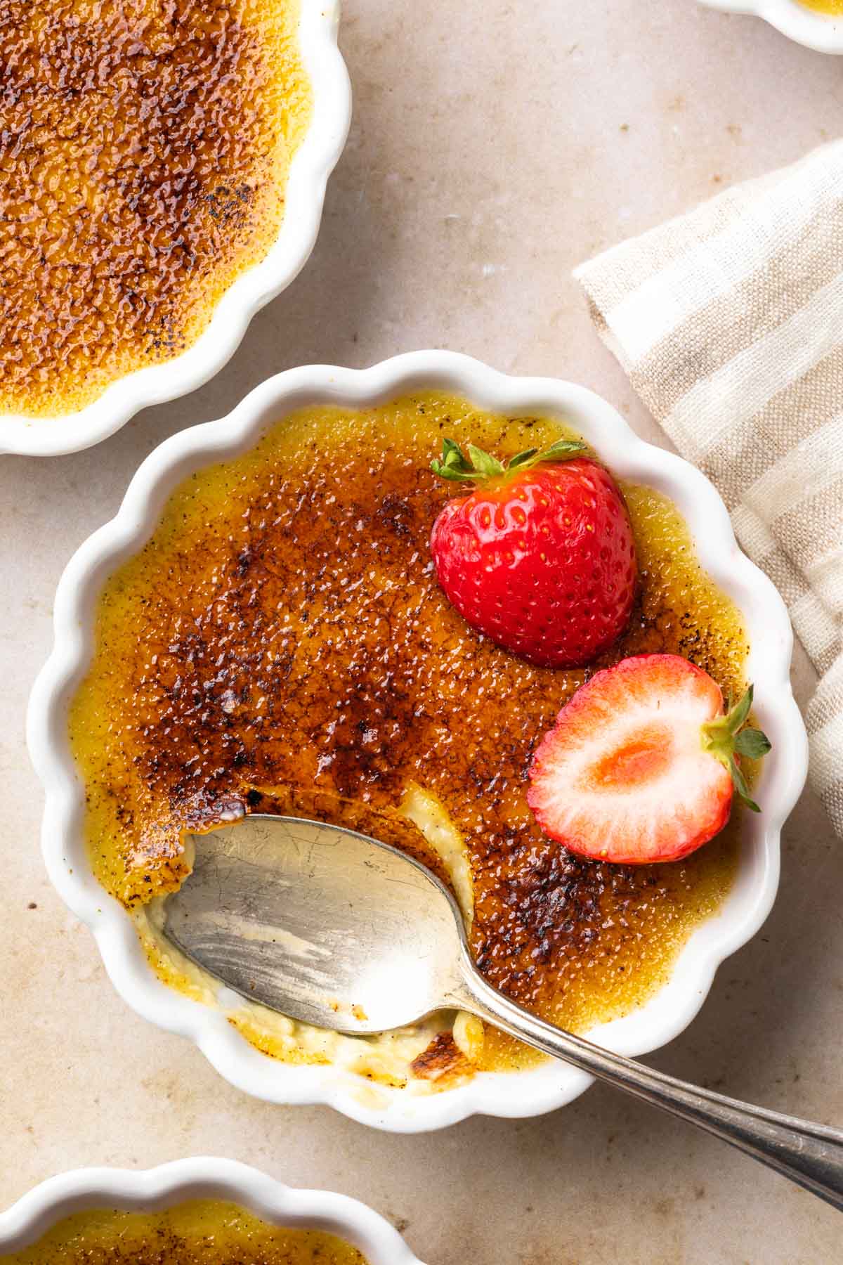 Close up of creme brulee in a dish with a spoonful removed garnished with fresh strawberries.
