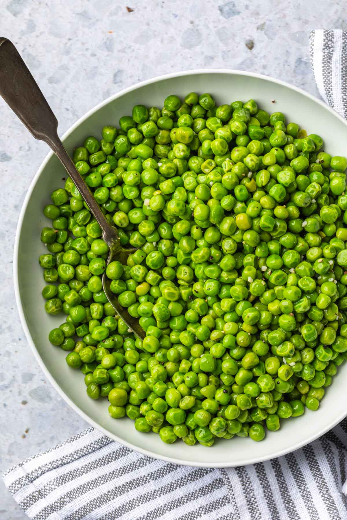 Overhead shot of a bowl of cooked peas with a spoon in them. 